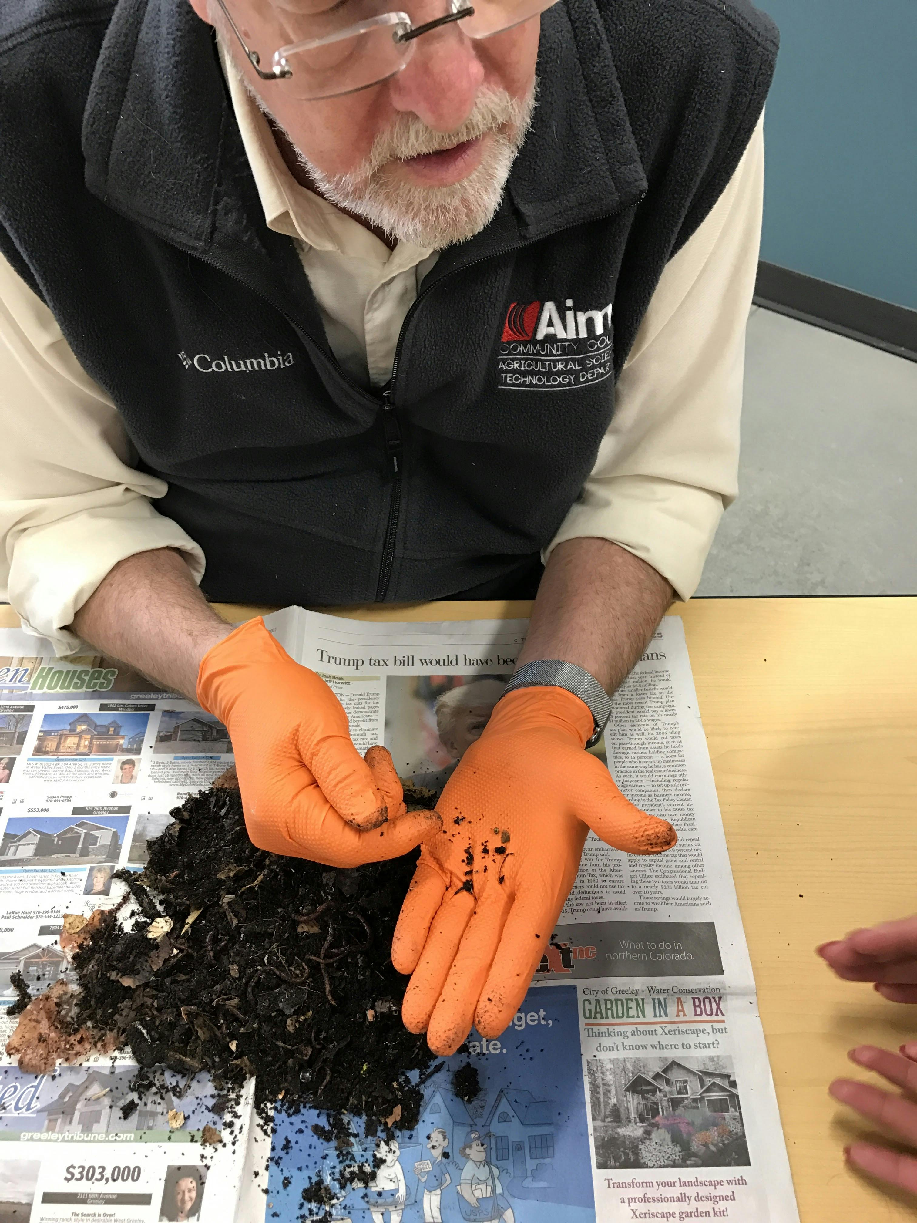 Teacher wearing Aims vest and orange latex gloves holding soil