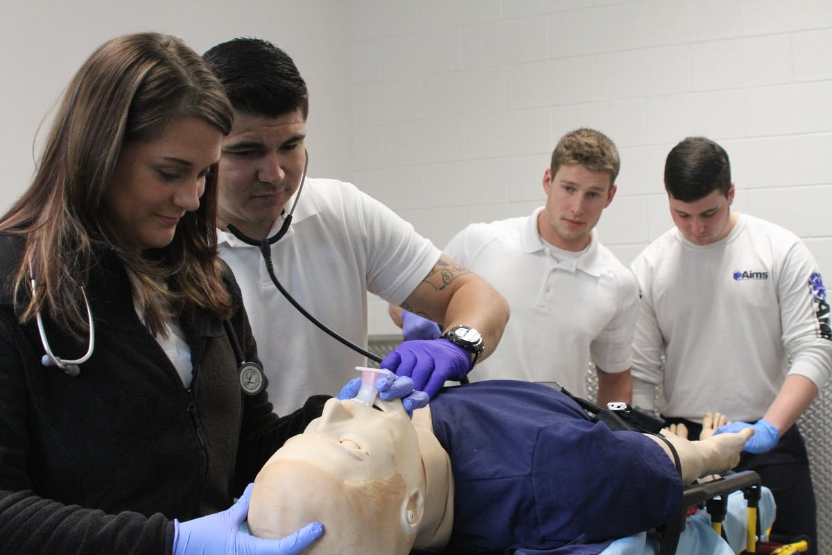 Two students practice on a dummy while two other students watch 