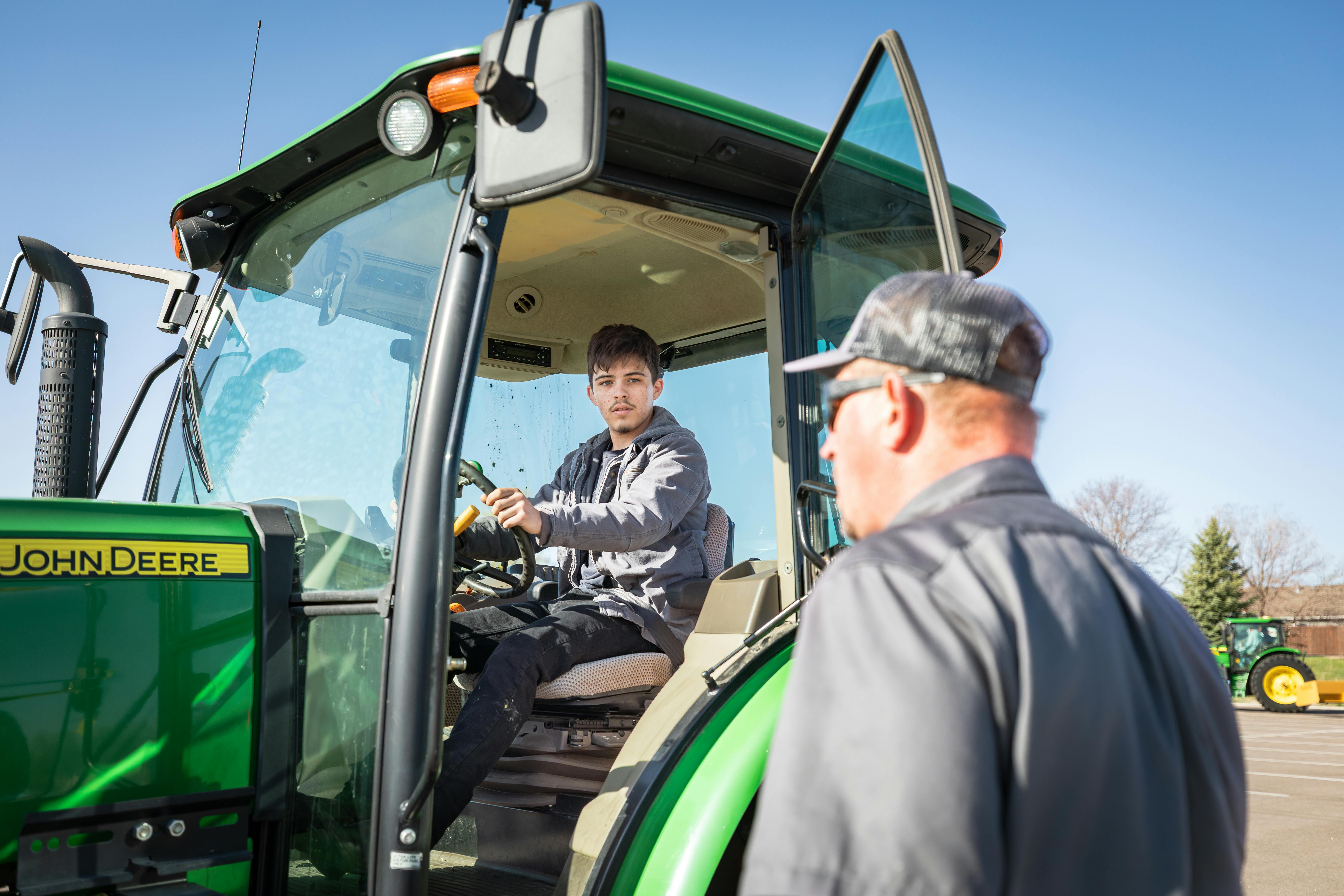 man sitting in driver's seat of tractor, teacher standing next to open door