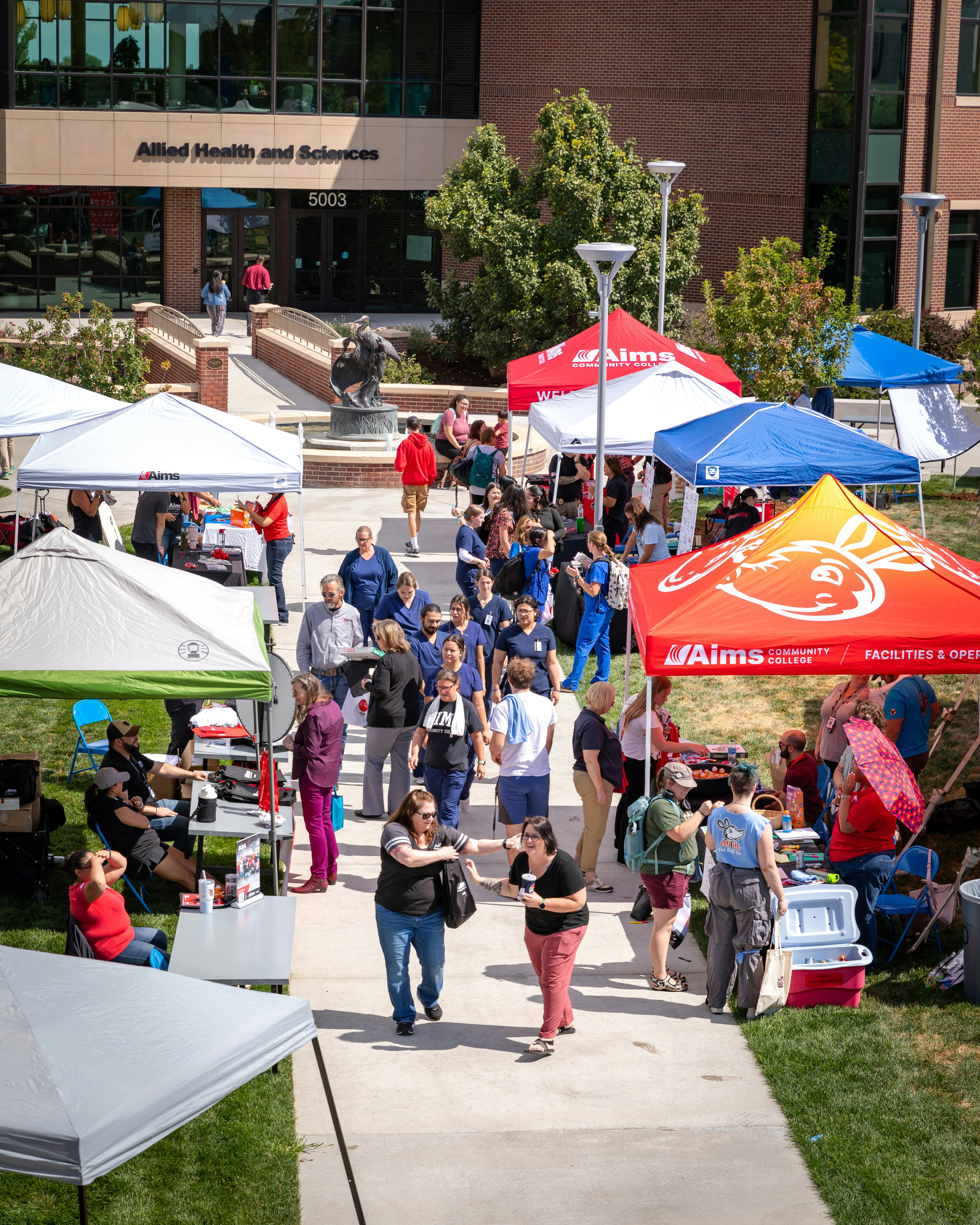 overhead shot of students outdoors walking between two rows of tents and tables 