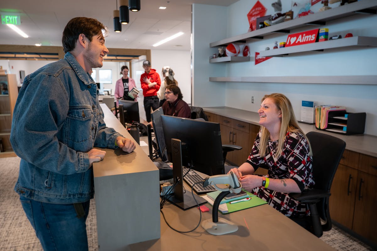 Student talks with a front desk employee in the Aims Learning Commons