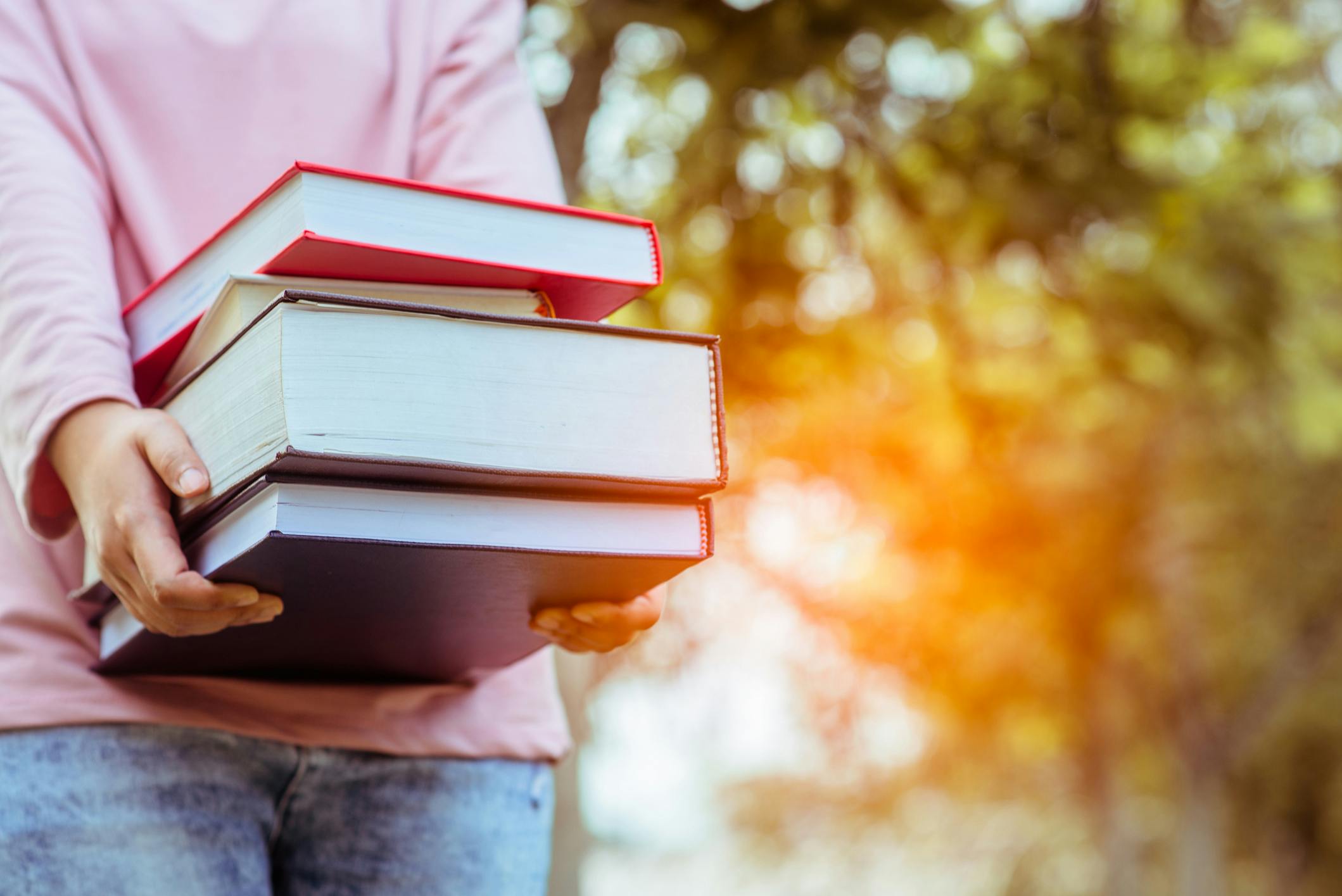 A student walking outdoors carrying a stack of textbooks