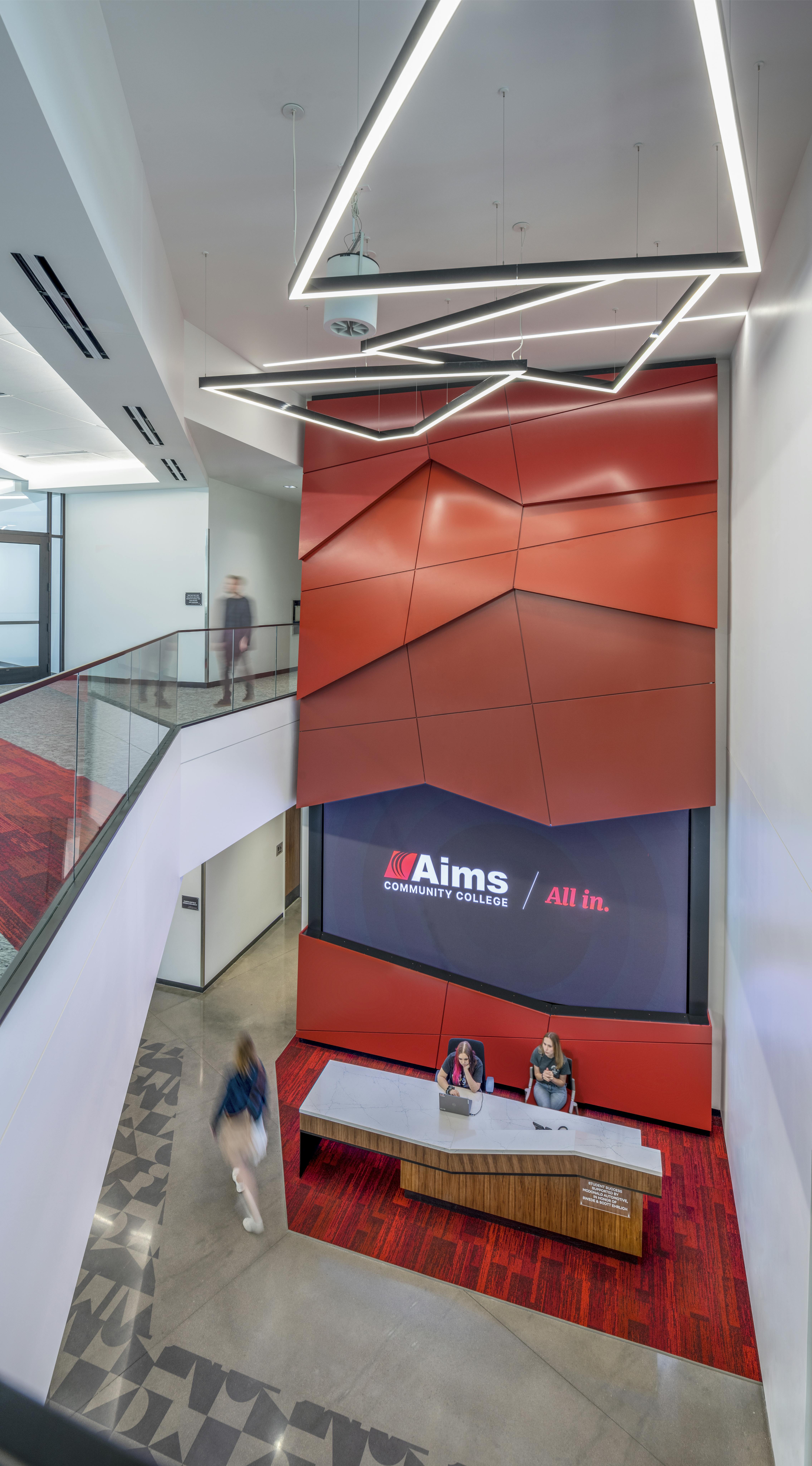 two students sitting at Navigation Station desk at Aims Welcome Center under Aims sign that says All In