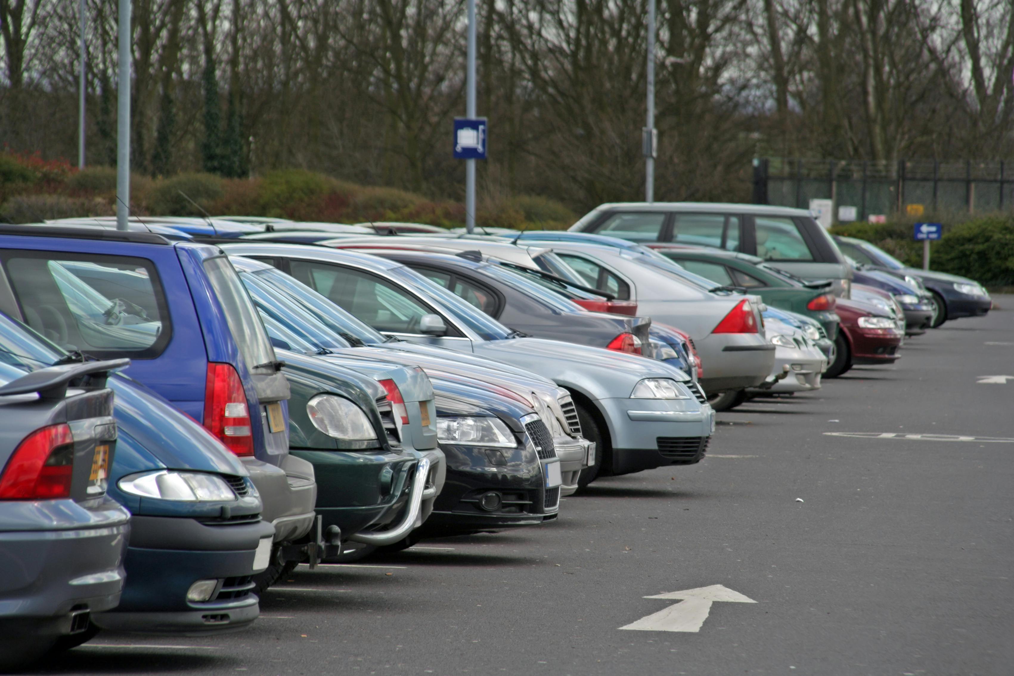 row of cars in a parking lot with white arrows painted on blacktop 