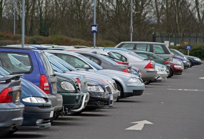 row of cars in a parking lot with white arrows painted on blacktop