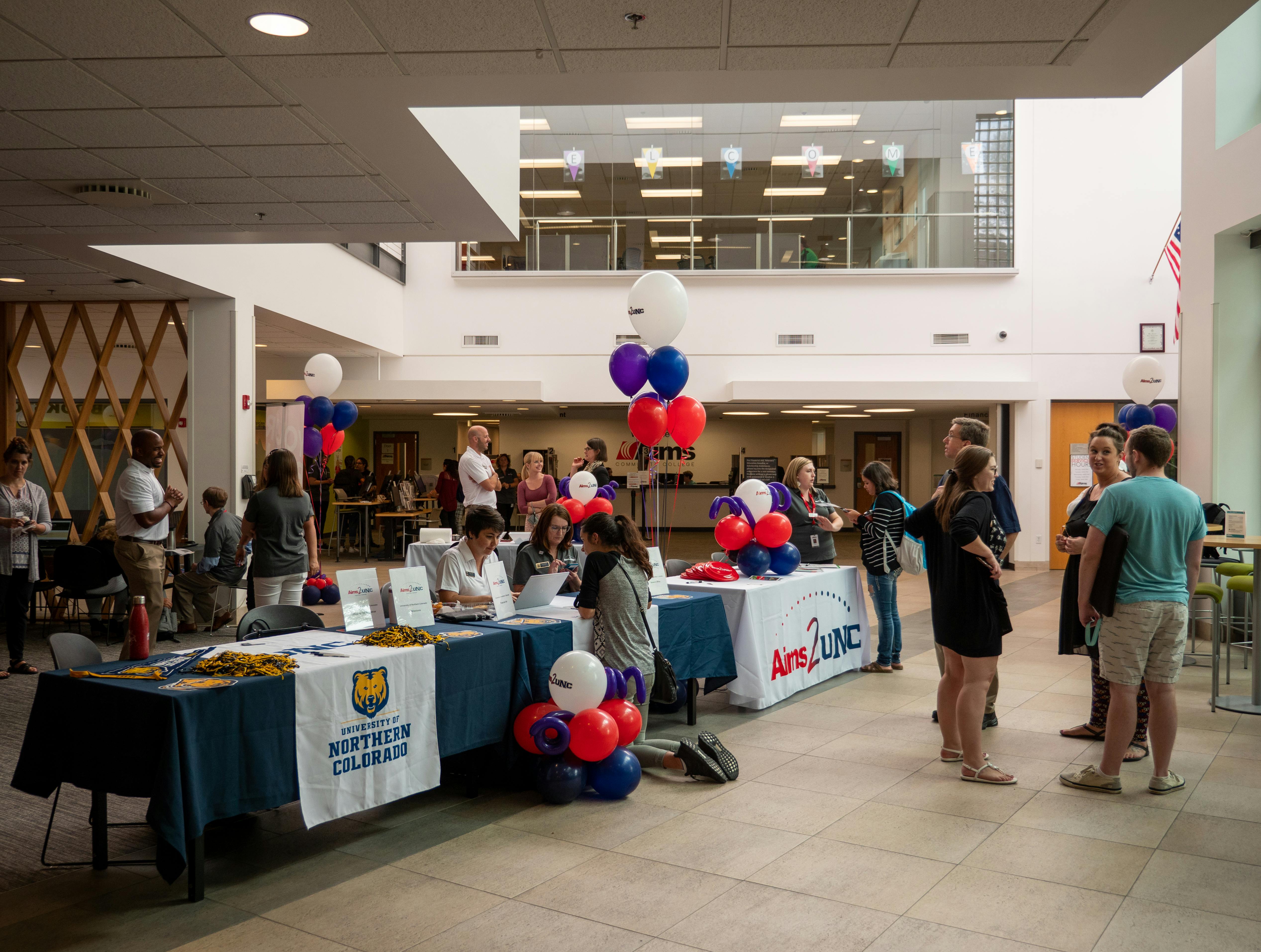 Students standing talking to people behind display tables for colleges at transfer fair