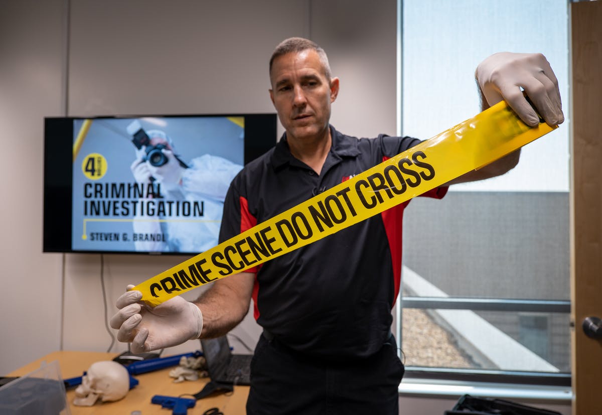 A professor stands holding up "Crime Scene Do Not Cross" tape