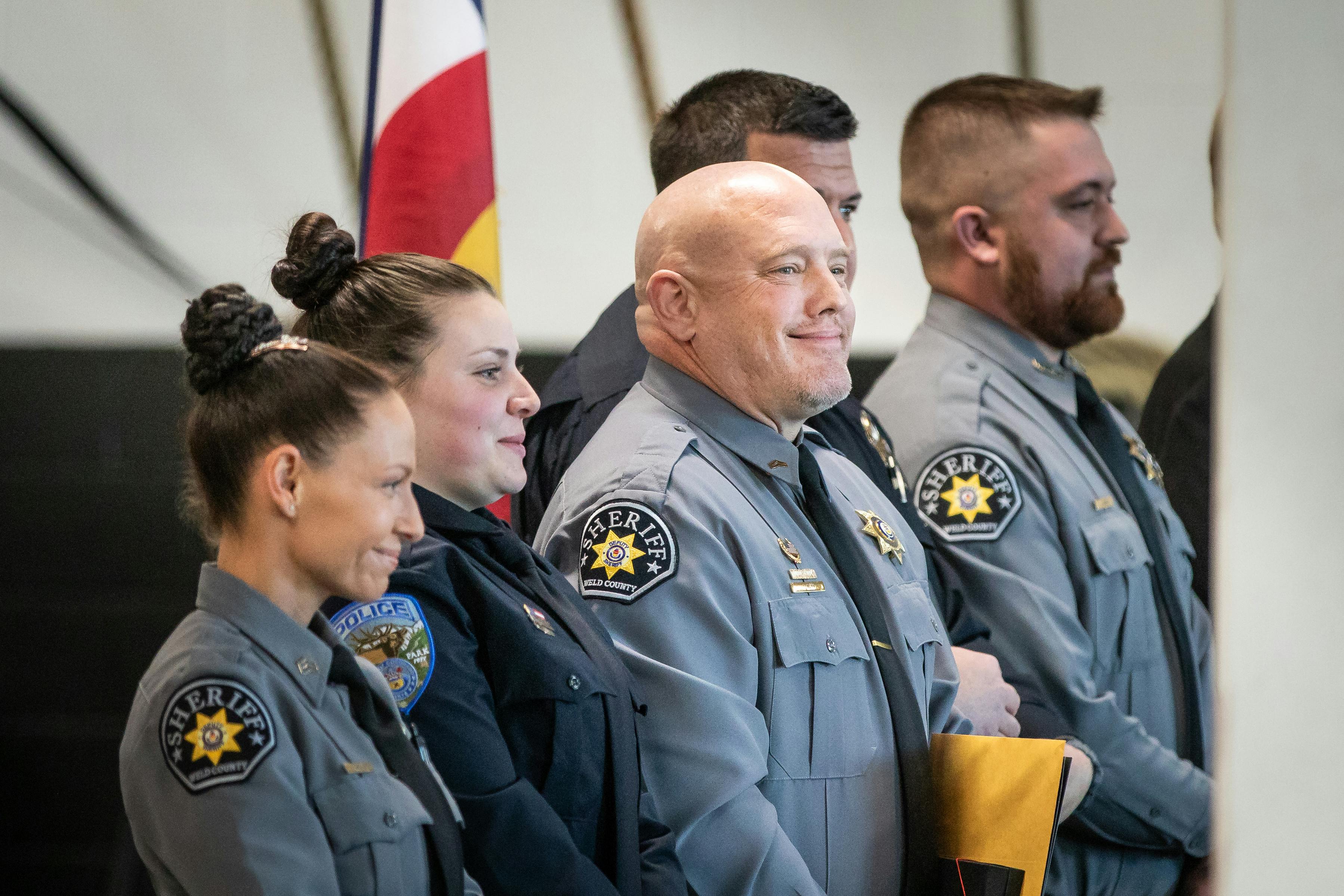 Four students in police officer uniform stand smiling at graduation