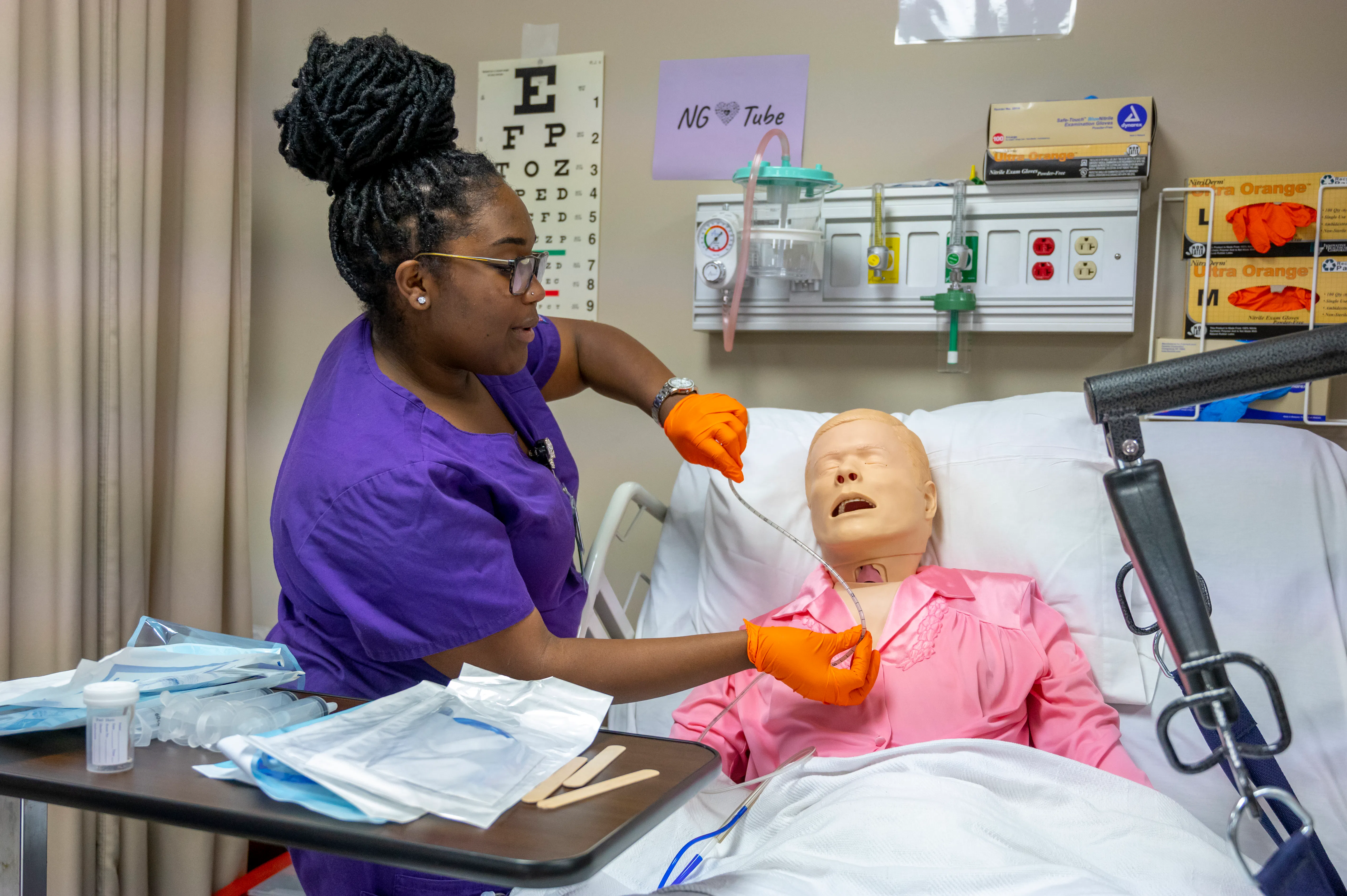 A nursing student practices NG tube insertion on a patient simulator in a clinical skills lab.