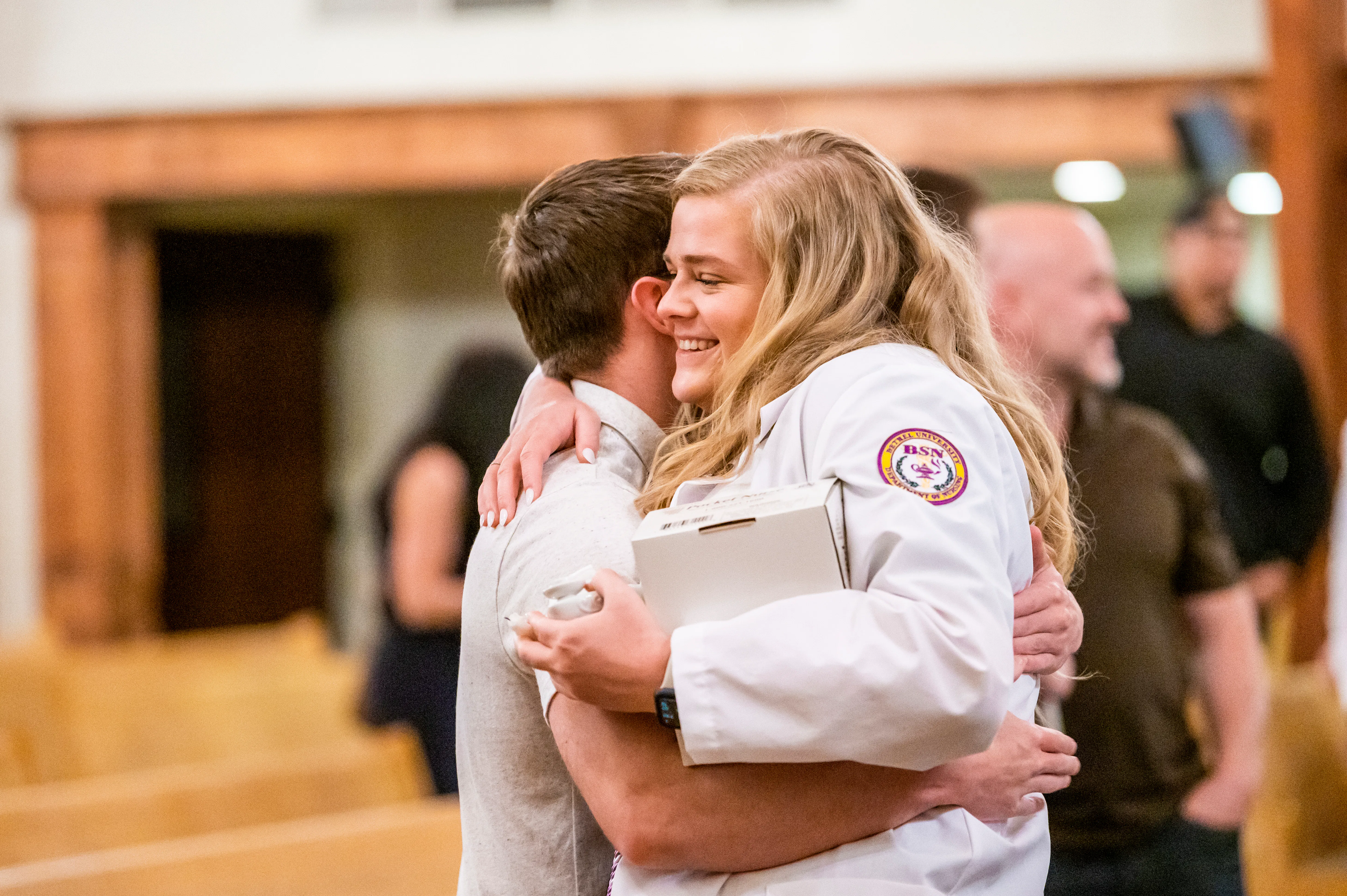 A Bethel University BSN nursing graduate smiles as she embraces a family member following her pinning ceremony.