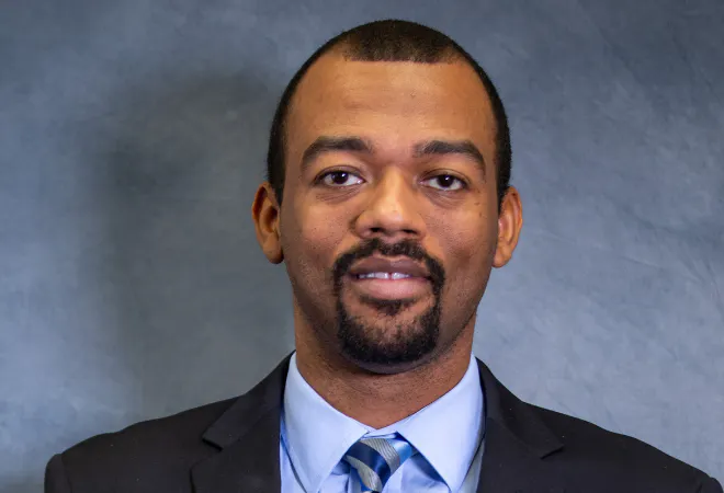Admissions Counselor, Dakarai Haughton, facing camera with blue background.