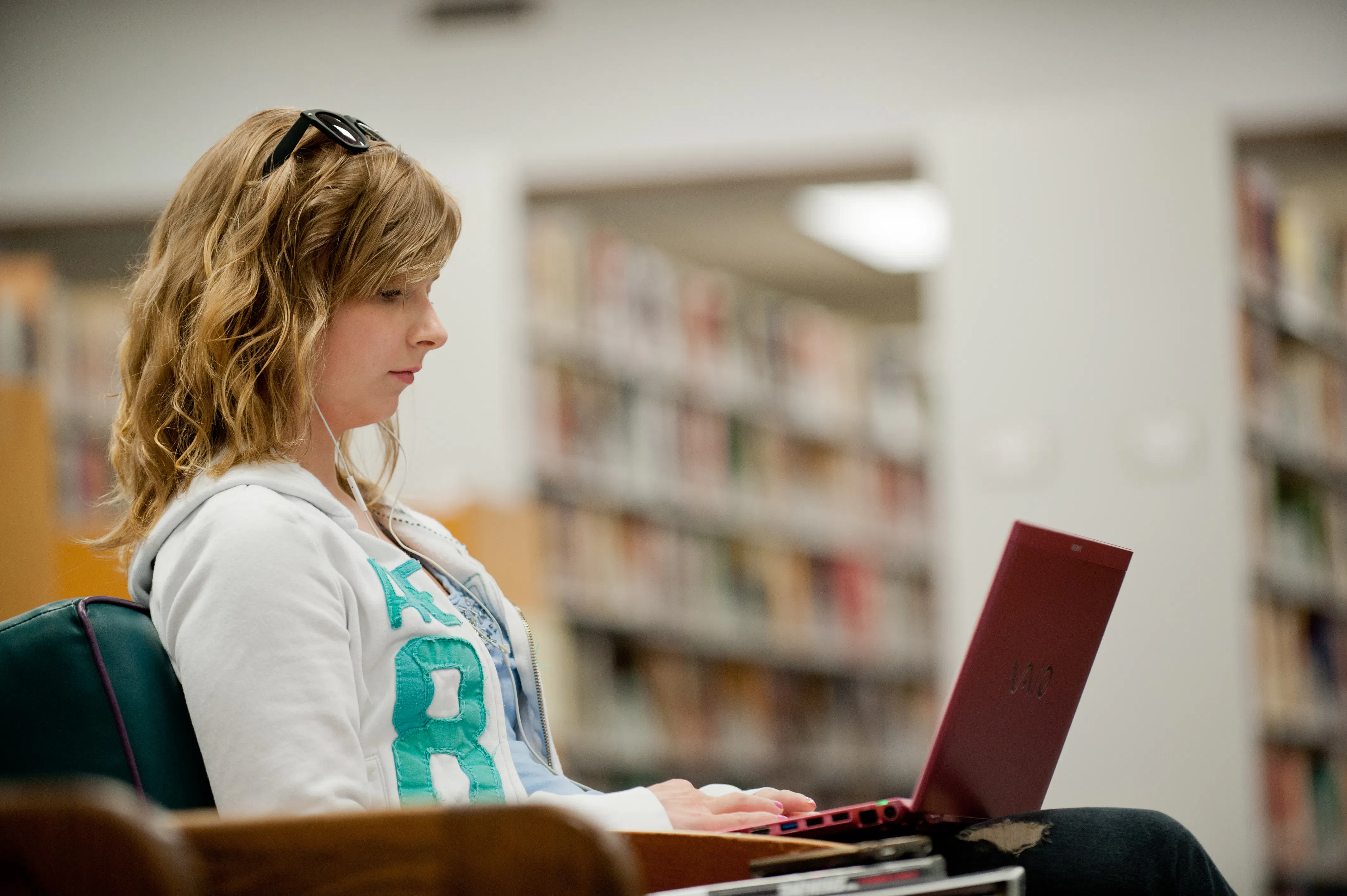Student studying on a red laptop in a campus library.