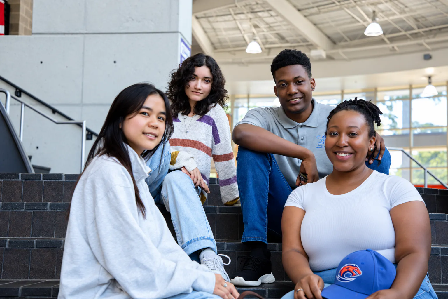 Four smiling students sit together on indoor campus steps in a bright student center.