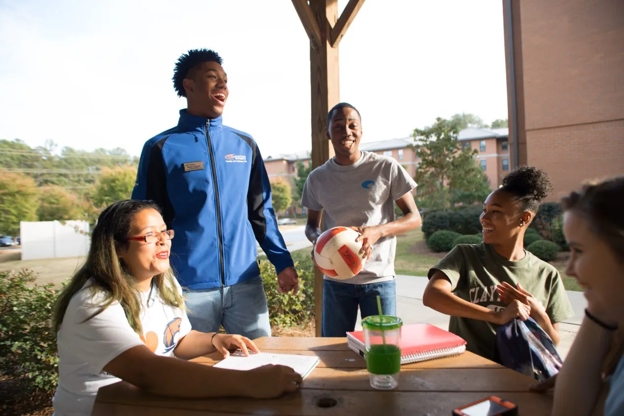 CSU students gather at an outdoor table near Laker Hall, smiling an laughing under a wooden structure.