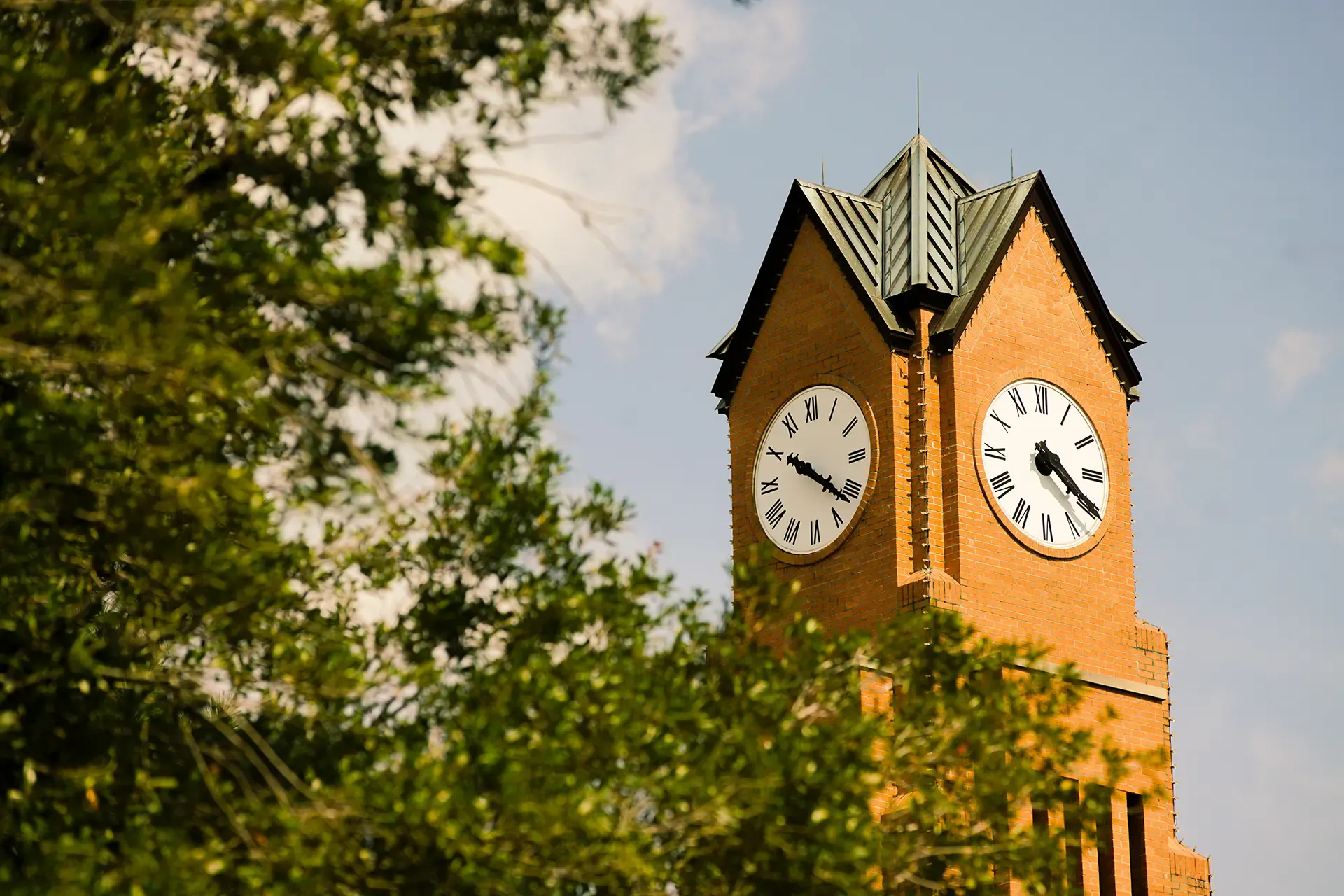 Columbus State University clock tower framed by trees against a blue sky.