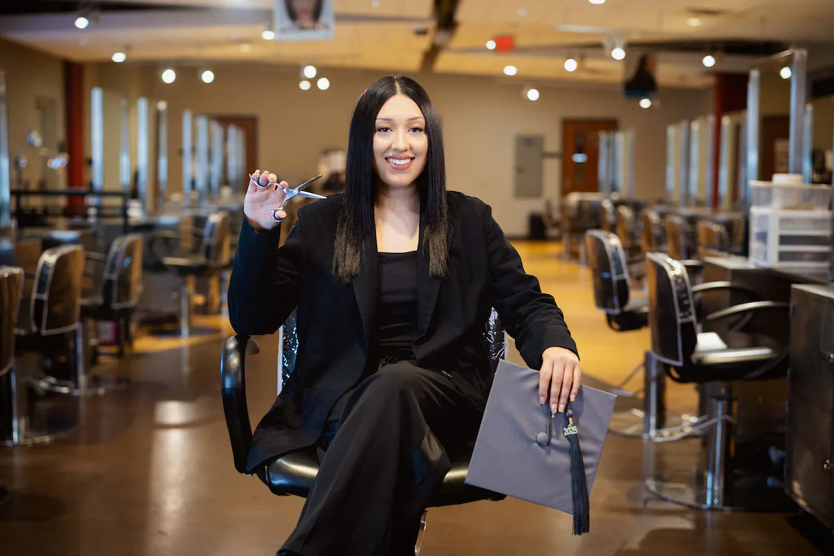Central Piedmont Community College cosmetology program graduate posing in an on campus salon  with a pair of scissors.