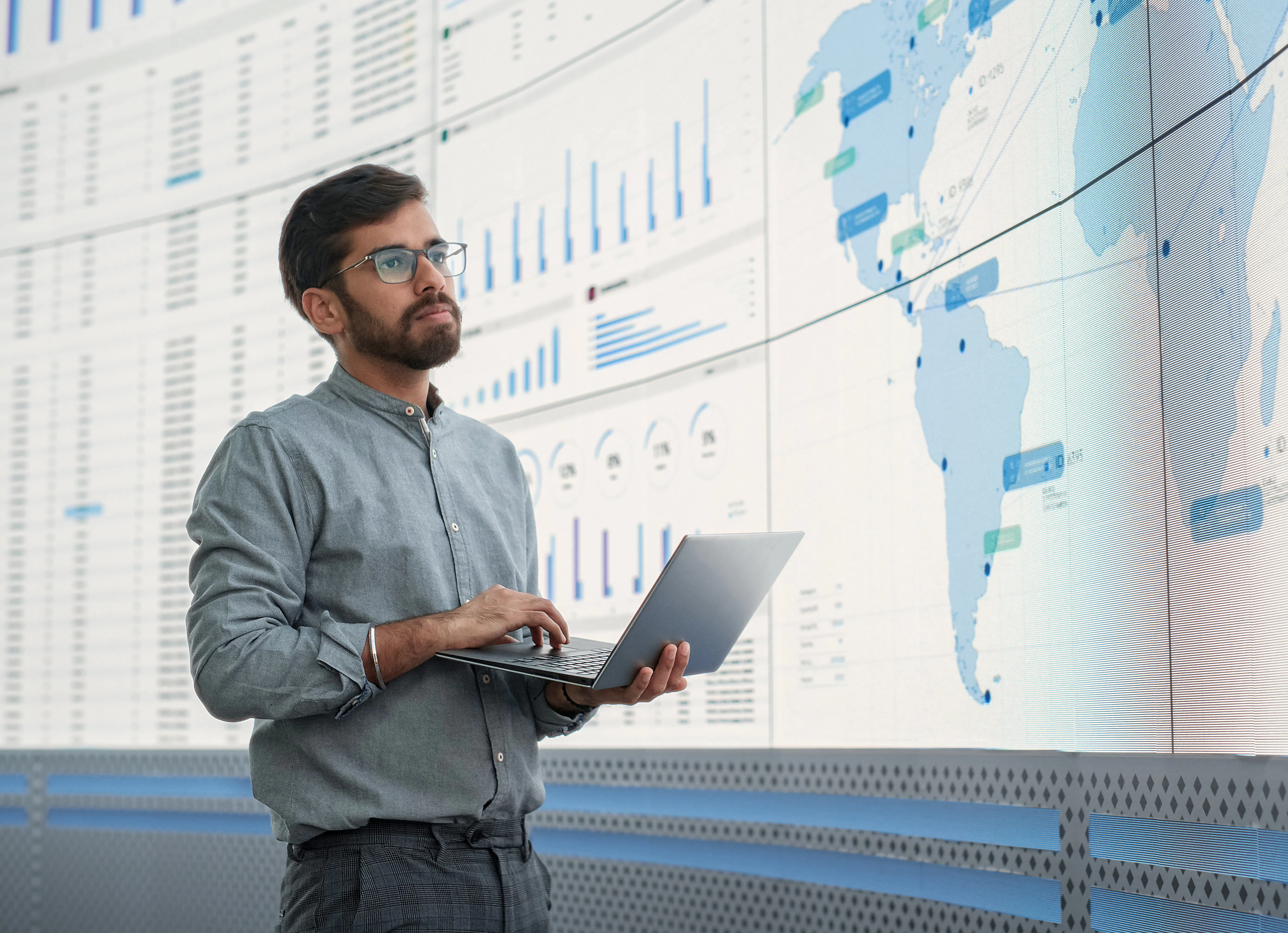 A data analyst in front of a wall of screens with various data charts.