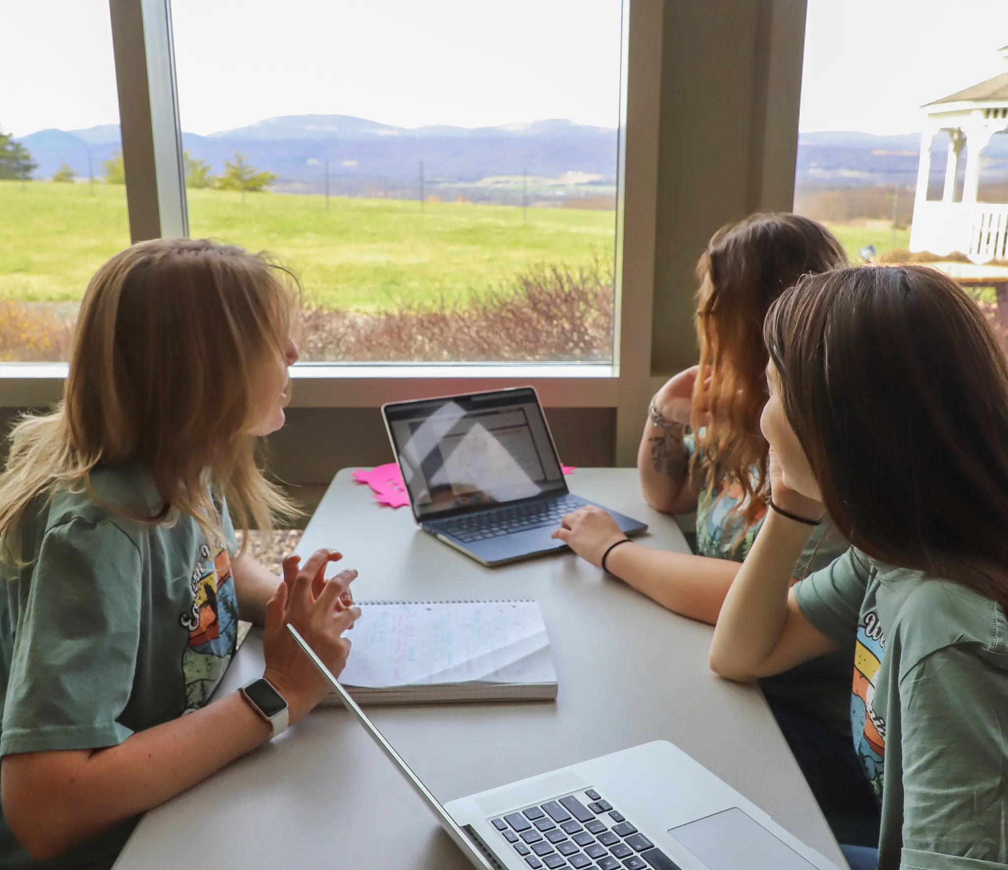 Three female students looking at laptop with notebooks in front of them on table.