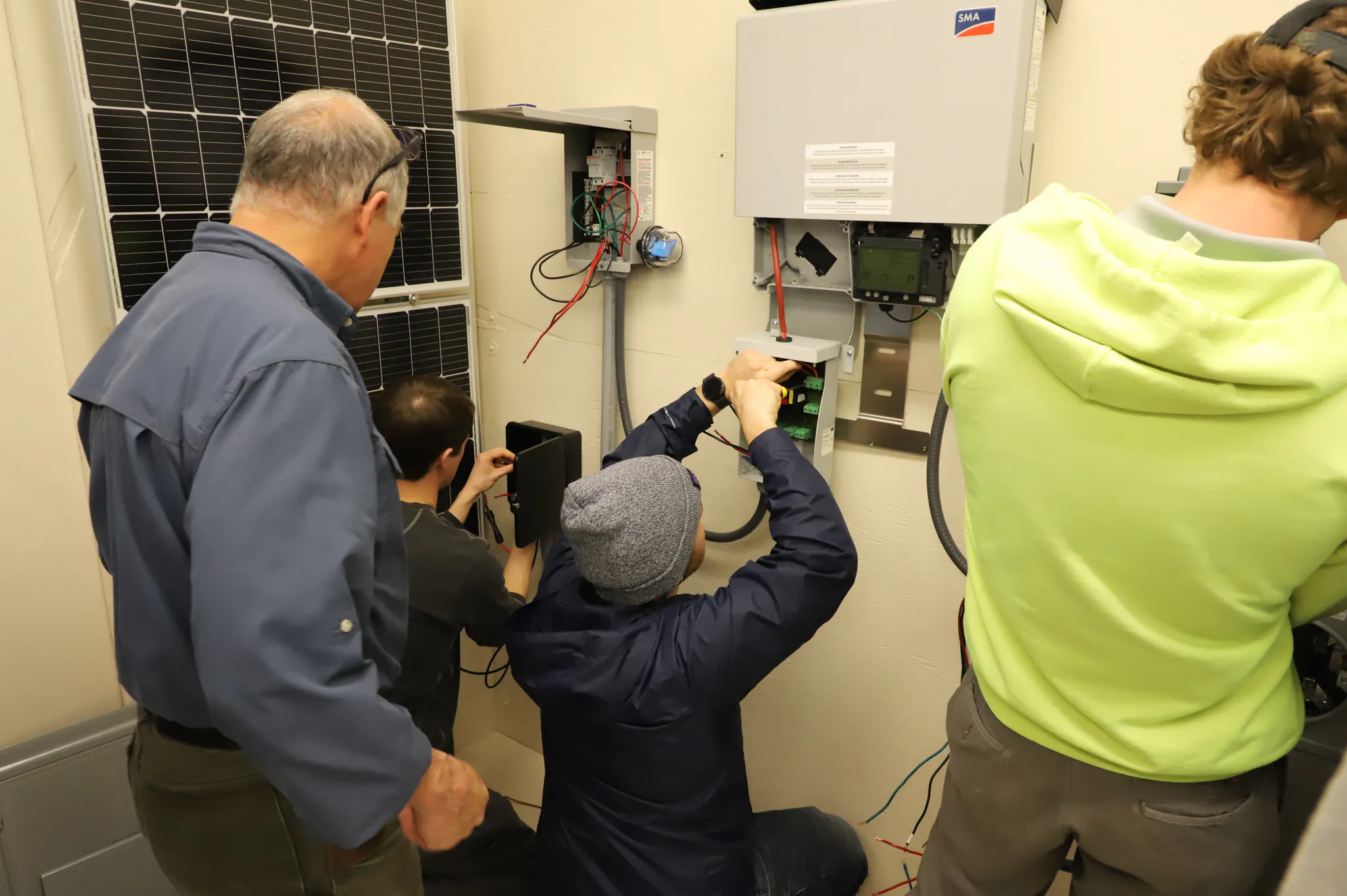 Four men working on electrical box with solar panel by them.