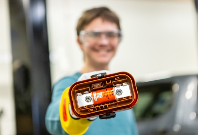 Student holding up a tool for electric vehicle repair.