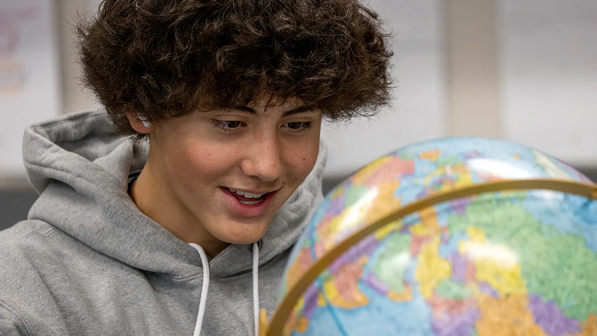 Student smiles as he inspects a globe in a physical science classroom.