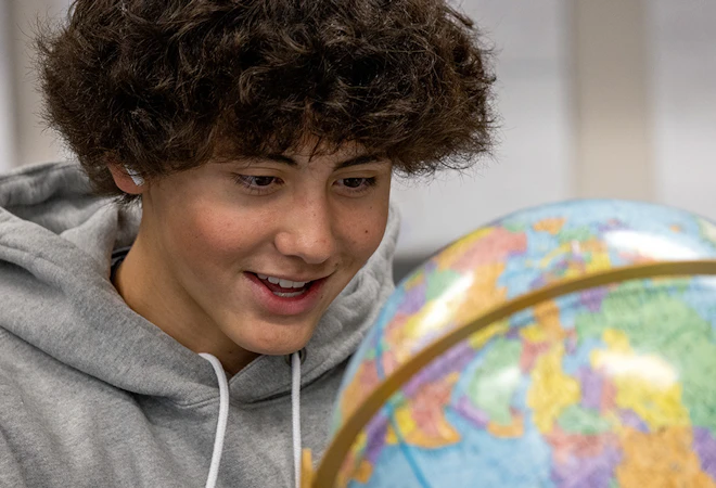 Student smiles as he inspects a globe in a physical science classroom.