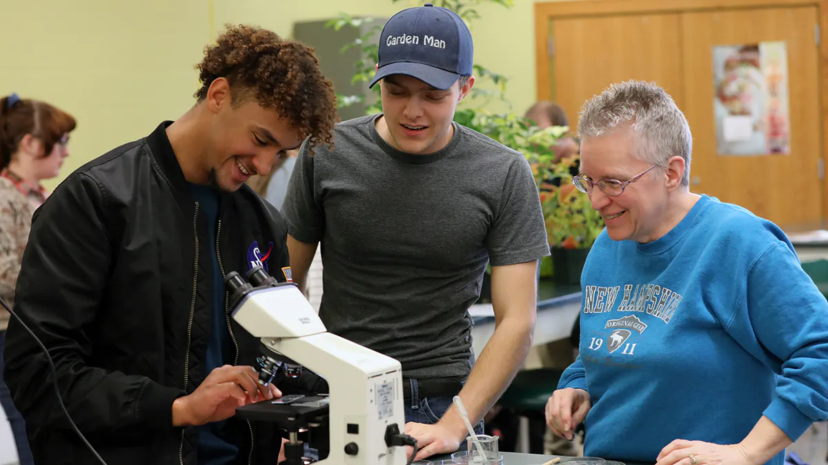 Three horticulture students examine slides under a microscope to identify plant fungus.