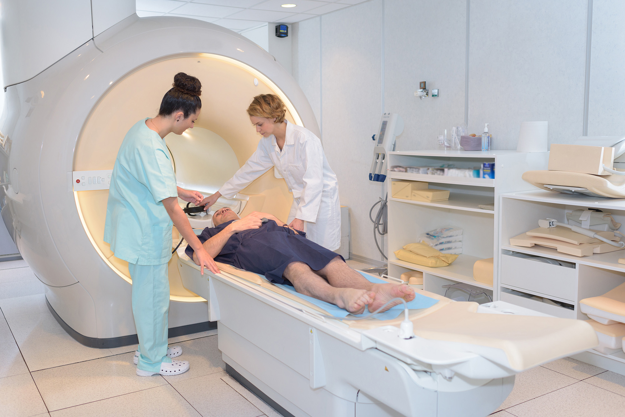 Two healthcare workers assisting a patient lying down in an MRI machine