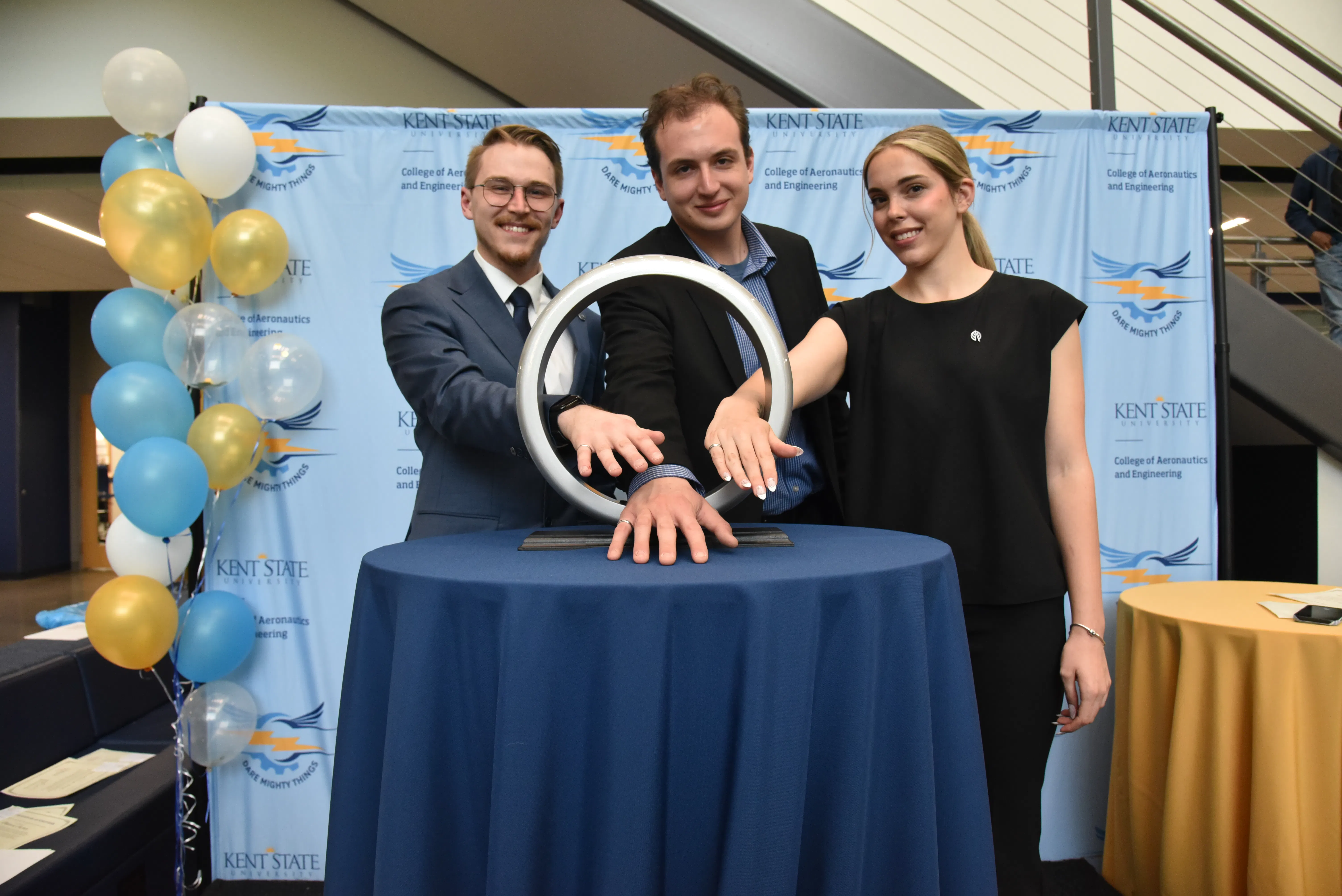 Three CAE students dressed in business attire show off their newly received engineer rings at the inaugural Order of the Engineer ceremony on May 1 by posing with their hands through the ceremonial ring prop.