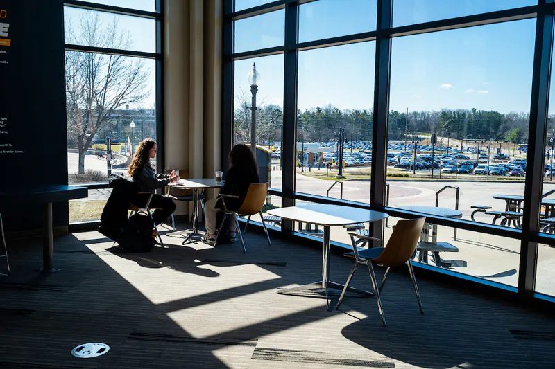 Two students sit and talk at a table inside a Kent State University building.