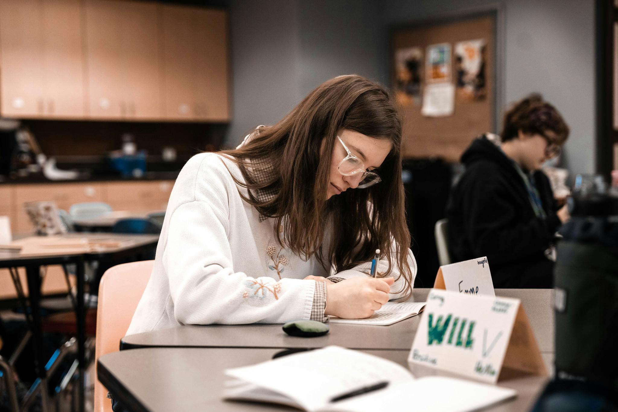 a female student sitting at a table writing on a notepad in class