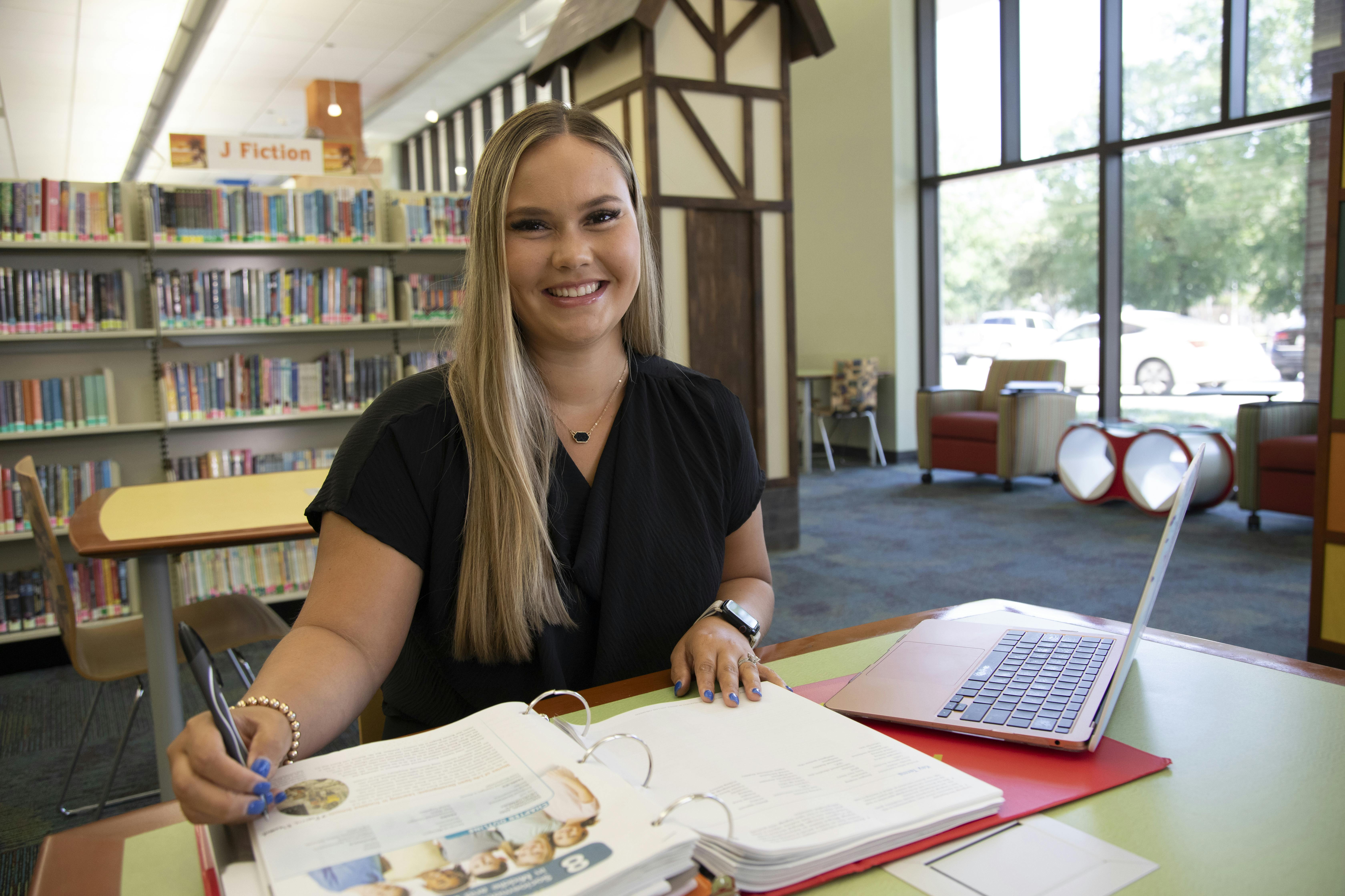 A woman sits at a laptop in a public library, earning her degree online.