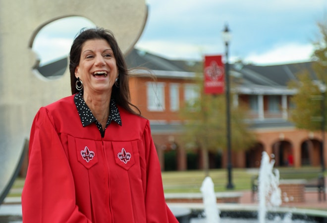 Health Promotion and Wellness graduate Karen Rana smiles in the University quad wearing her graduation gown.