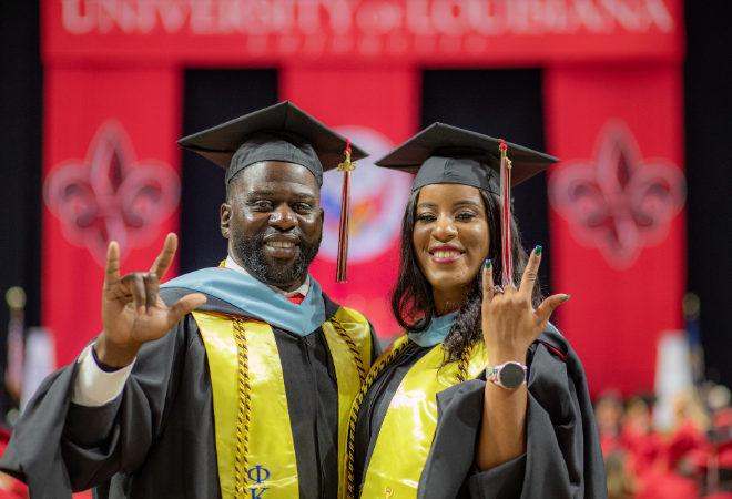 Kreig and Rekeisha Triggs hold up the UL Lafayette hand symbol in graduation regalia during commencement ceremonies.