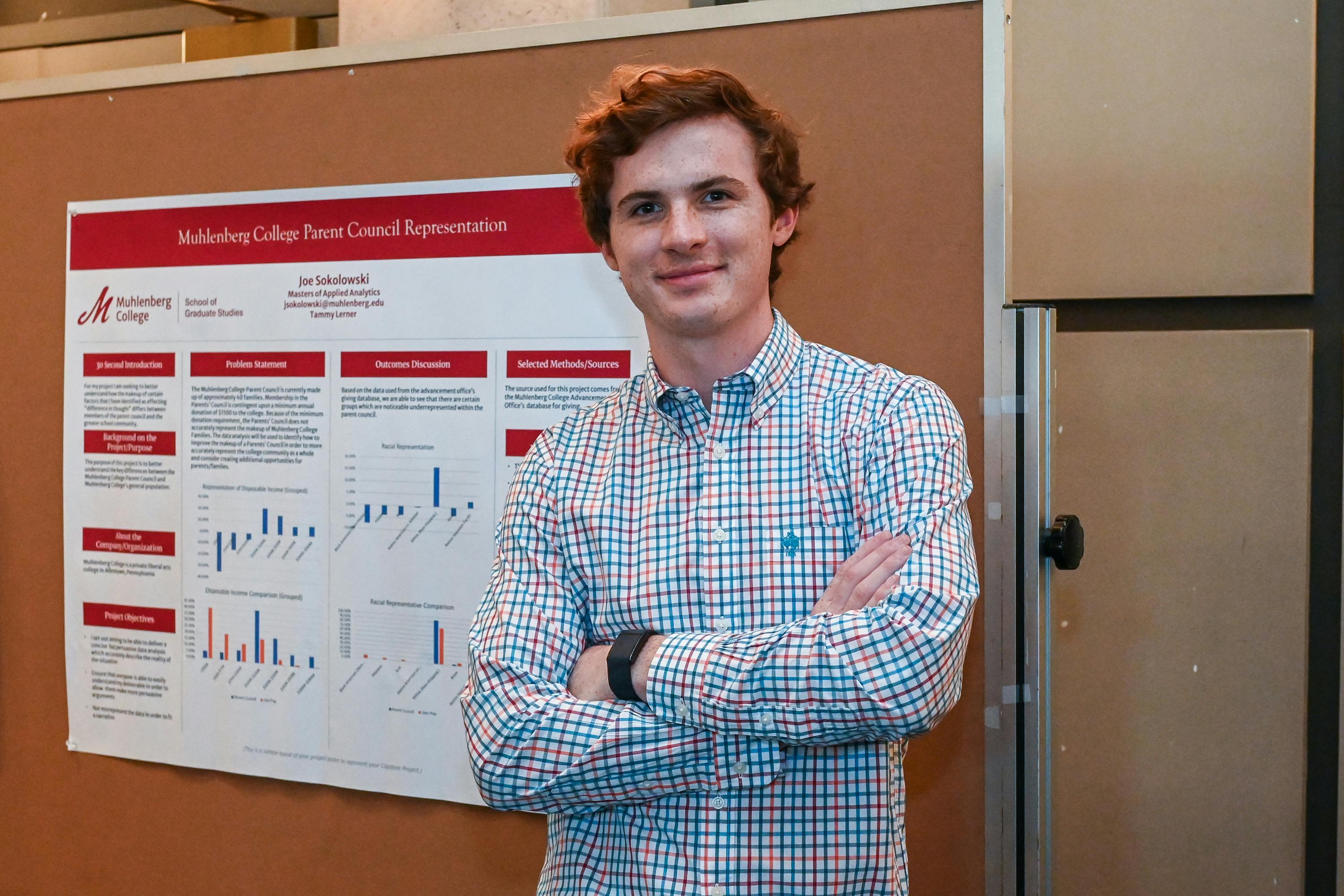 a student standing in front of a poster with his arms folded.