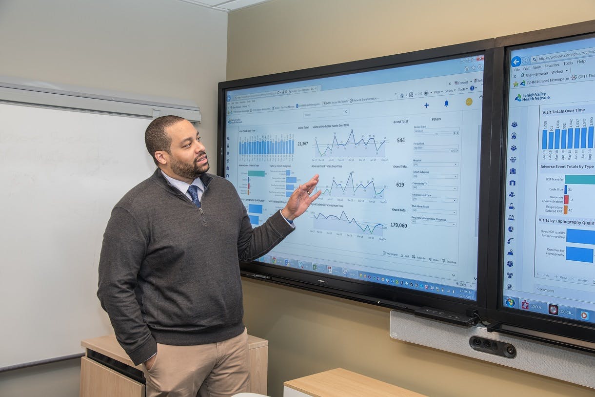 Student standing in front of two monitors presenting graphs of data
