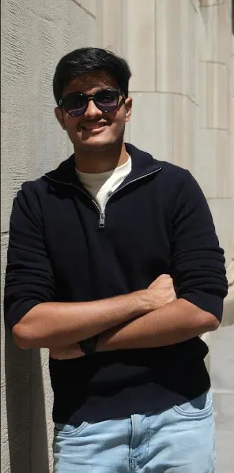 Hemil Mheta, a recent alum, is leaning against a wall on a busy city street.