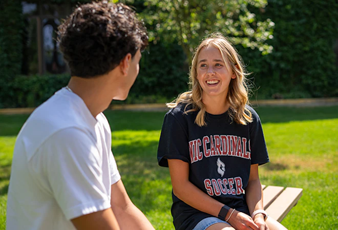 Two students talking on a bench outside