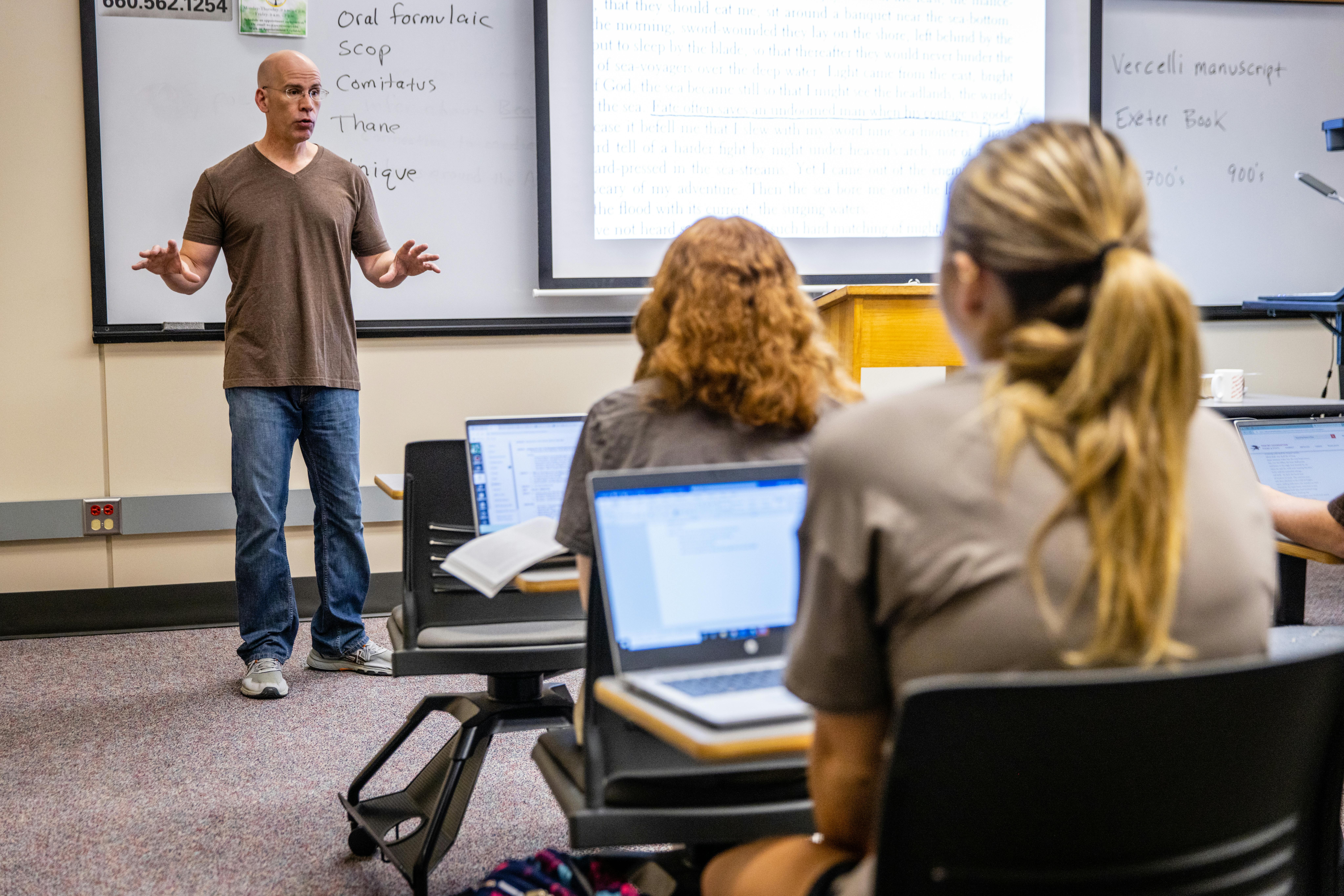 A professor talks in front of an english class with expressive hands.