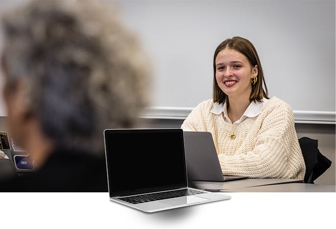 A student listens and smiles in English class while sitting in front of a laptop