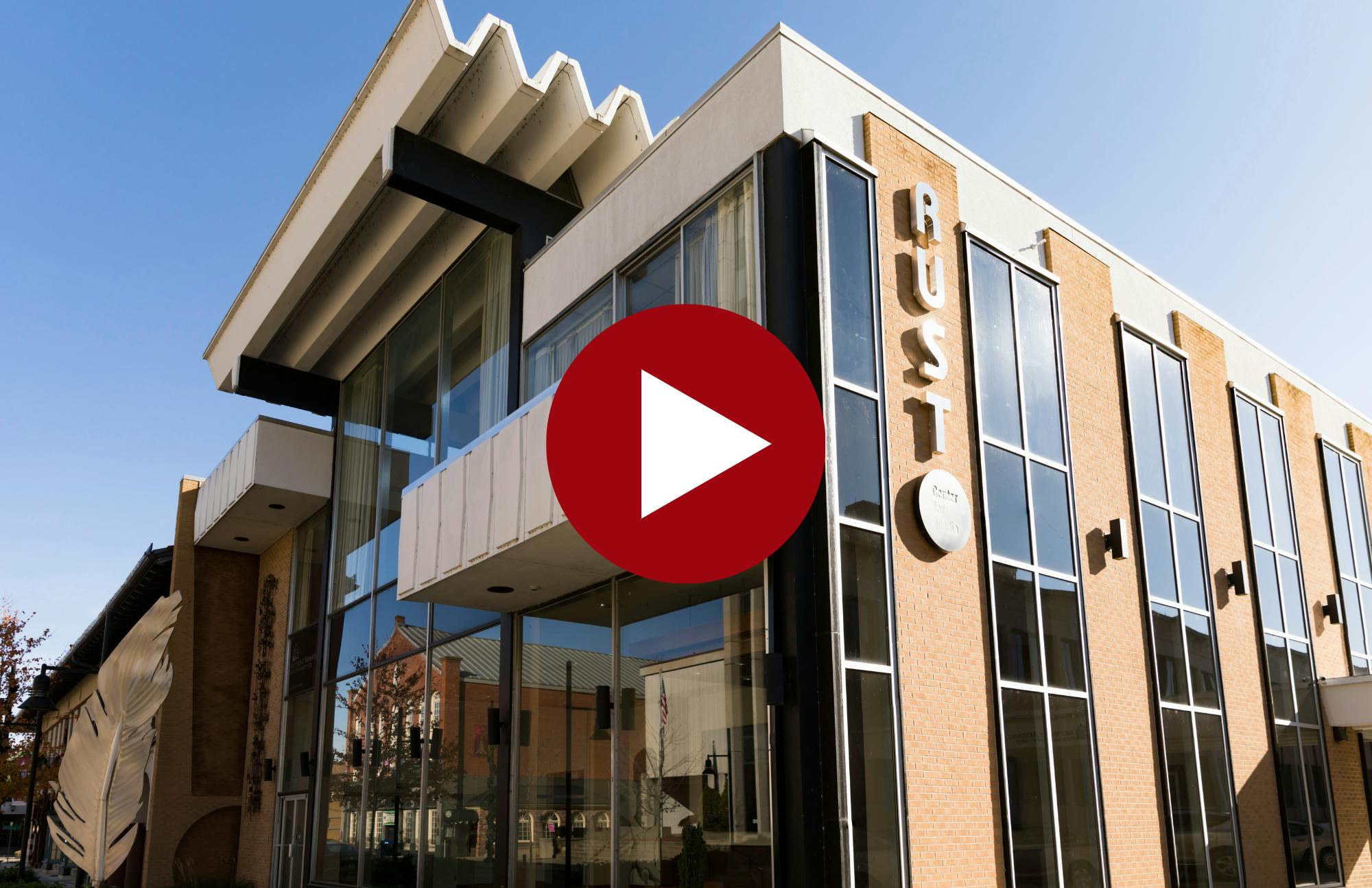 red play button overtop an image of the exterior of the Rust Center for Media building