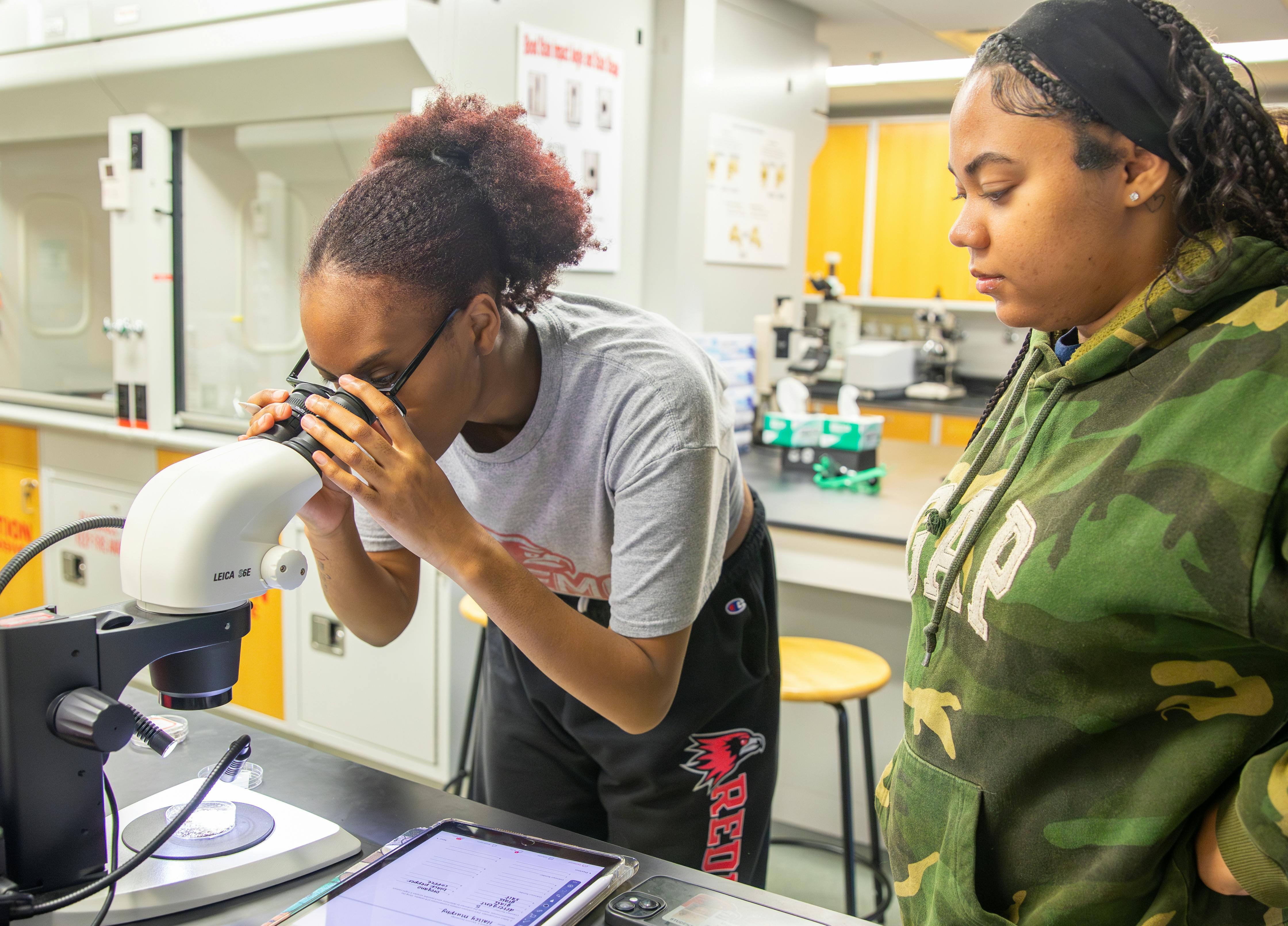 two students analyze forensic evidence through a telescope