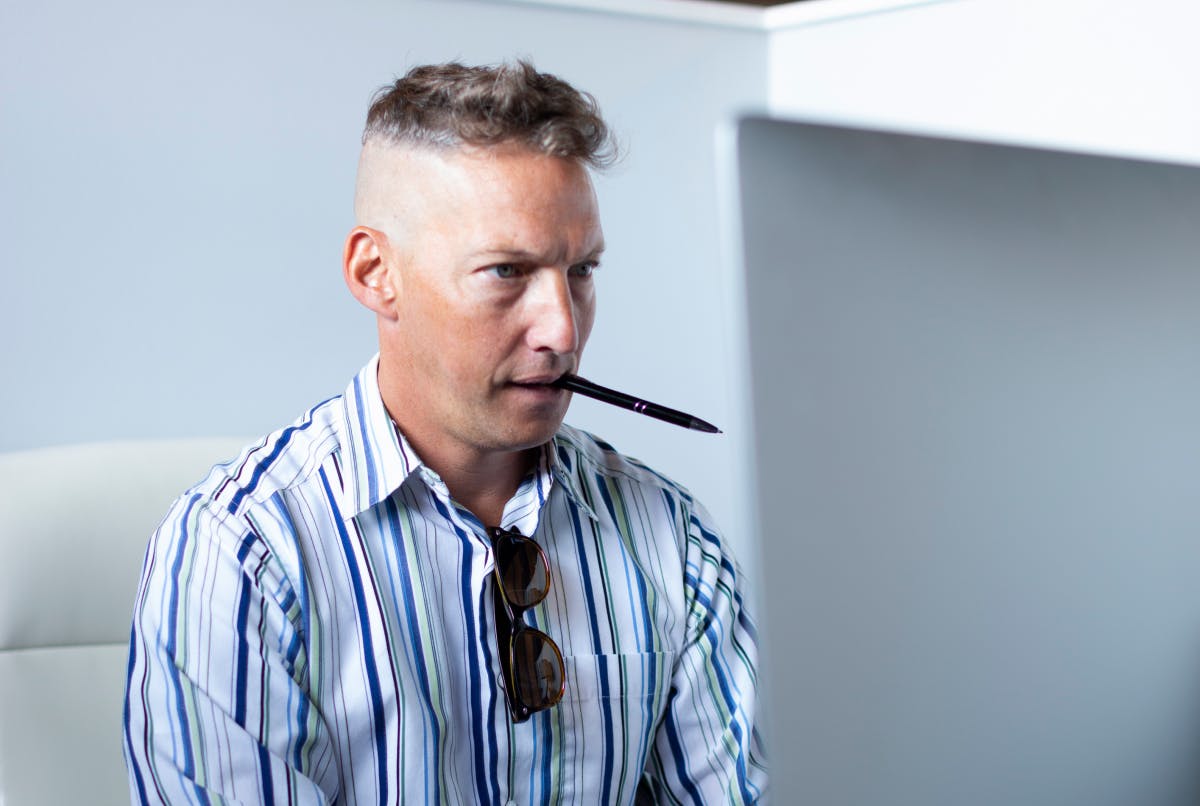 Man focused on computer with a pen in his mouth.