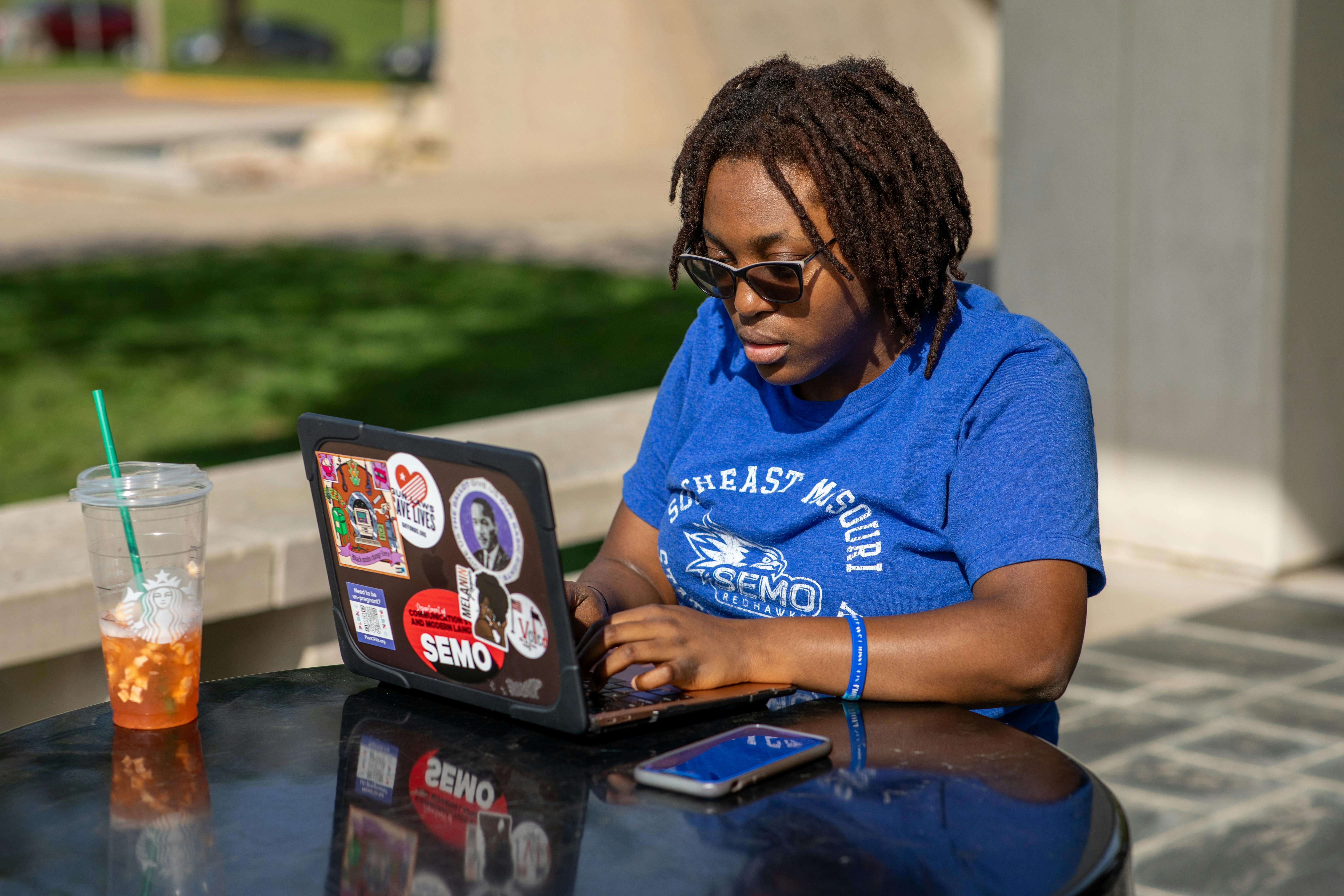 a student works on her laptop at an outdoor bench on campus. 