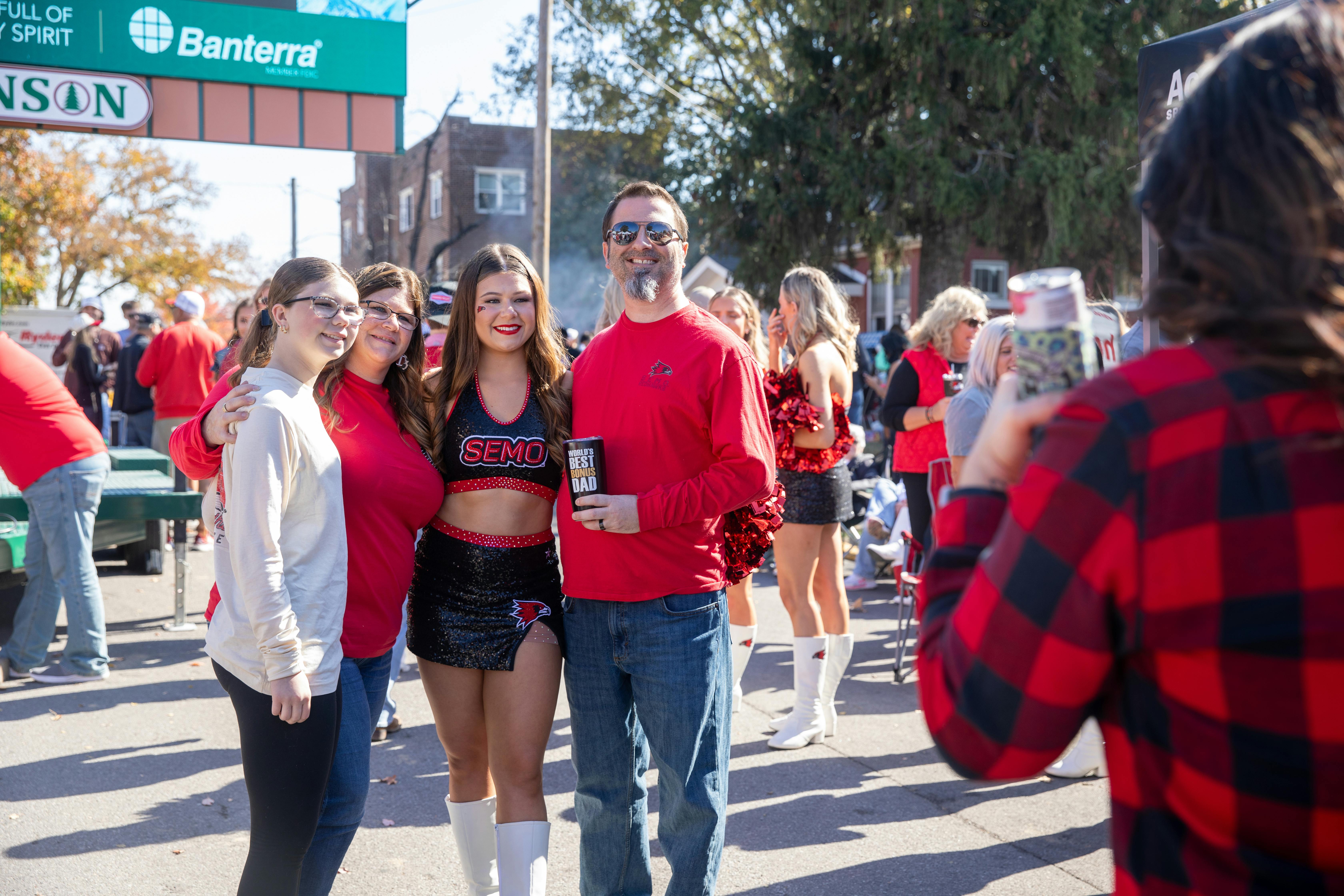 A family in Redhawk gear poses for a photo with their daughter wearing a SEMO cheerleading outfit after the homecoming parade.  