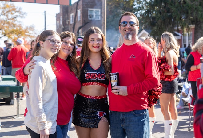 A family in Redhawk gear poses for a photo with their daughter wearing a SEMO cheerleading outfit after the homecoming parade.