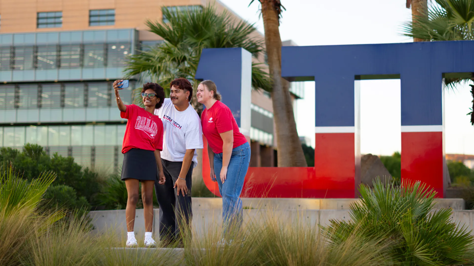 Students taking a selfie in front of Utah Tech University landmark "UT" with blue and red colors. Holland Centennial Commons Library in the background