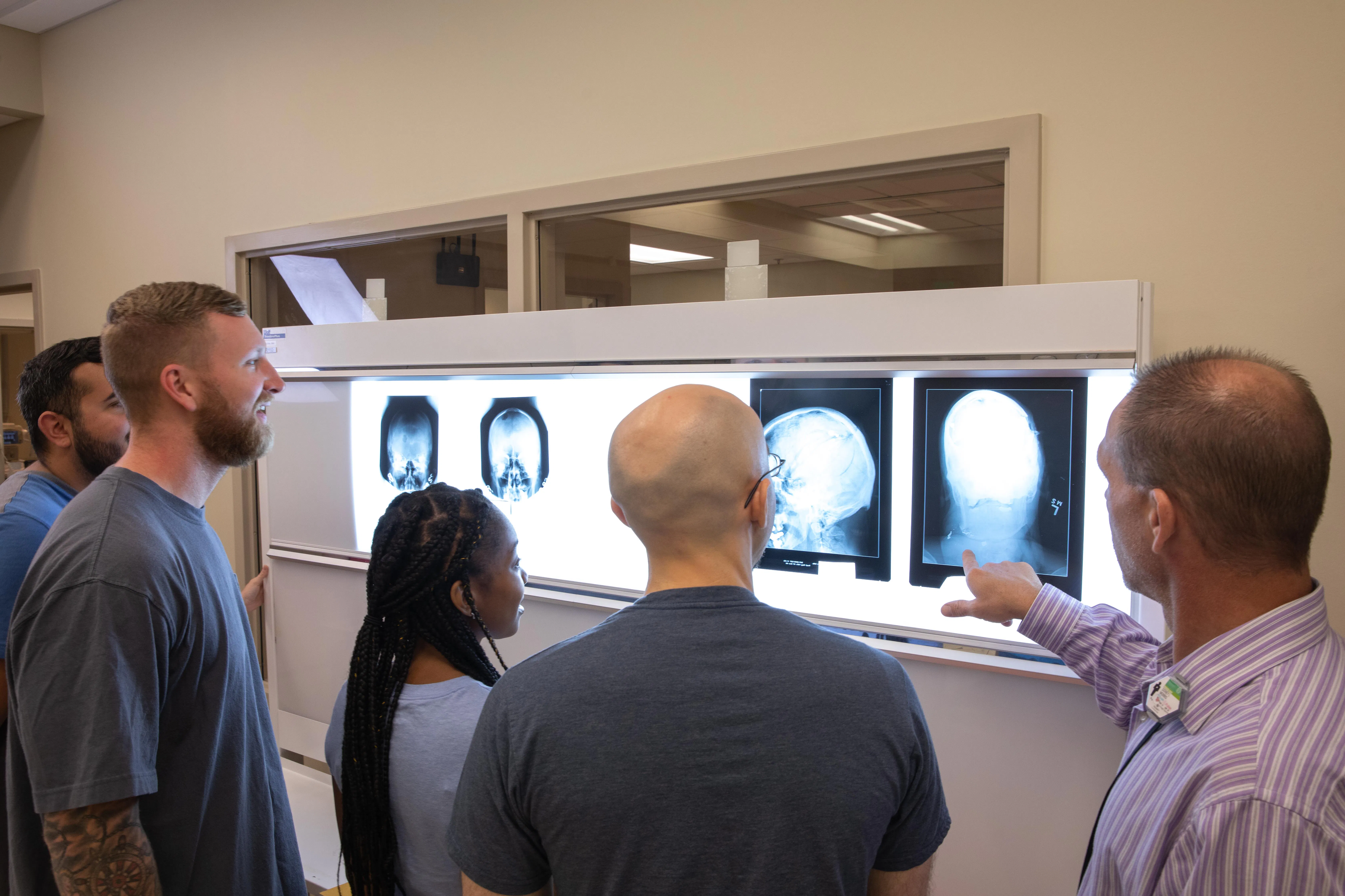 Wake Tech radiography students stand with an instructor reviewing X-ray images displayed on a lightboard in a medical imaging classroom.