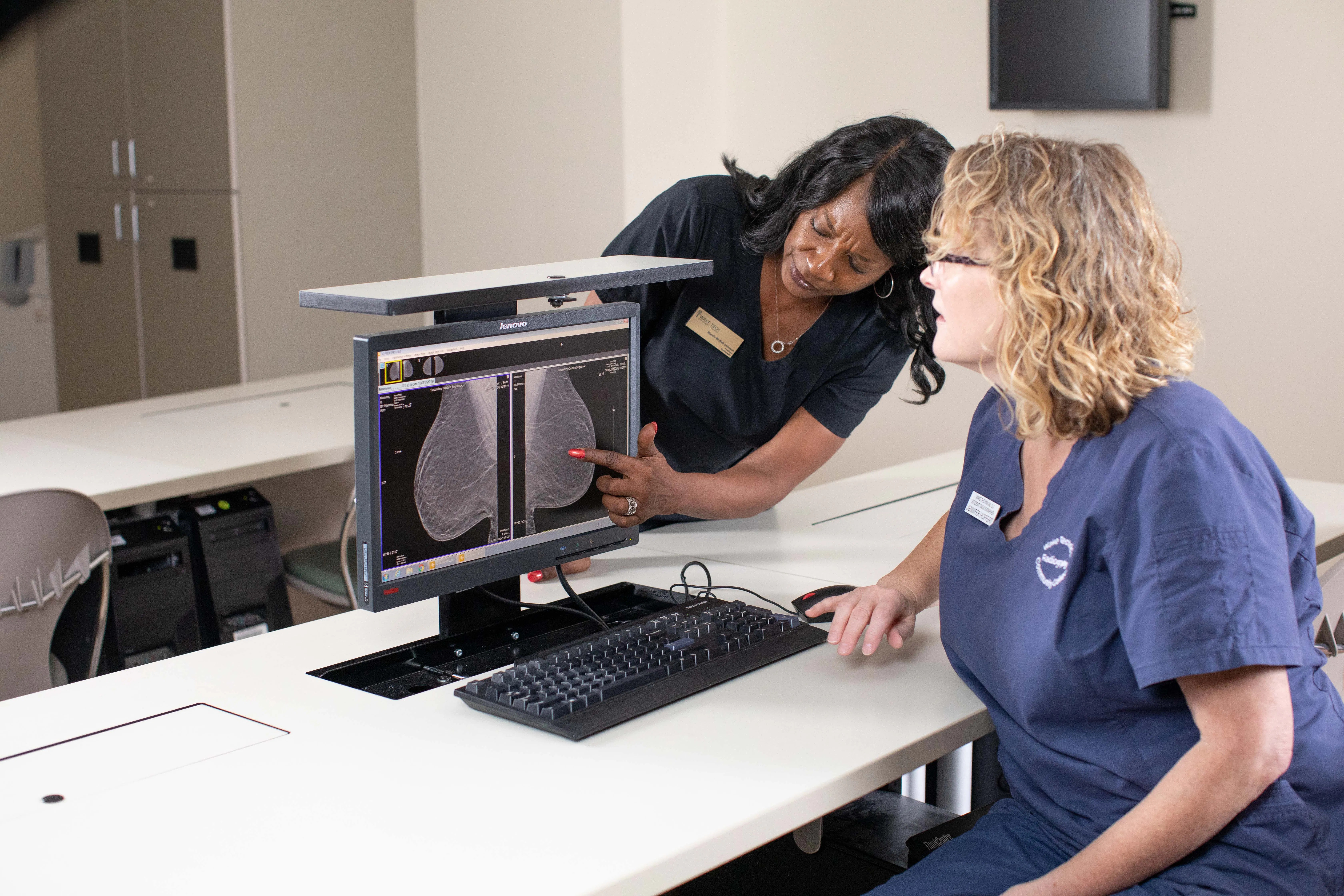 Wake Tech mammography students review breast imaging scans on a computer monitor in a medical imaging lab, with one student pointing to details on the screen while the other looks on.