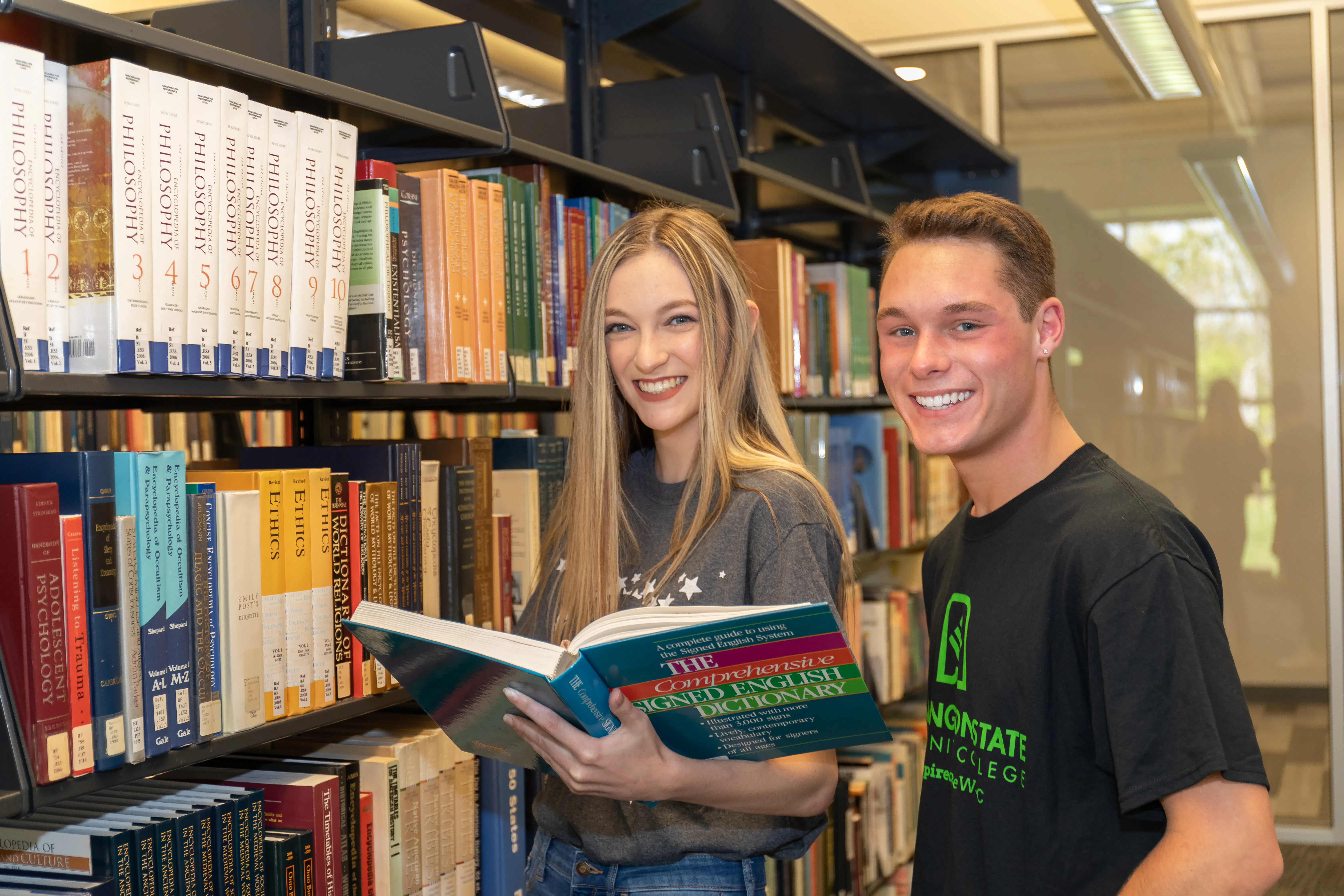 two students standing in front of the bookshelves reading in a library